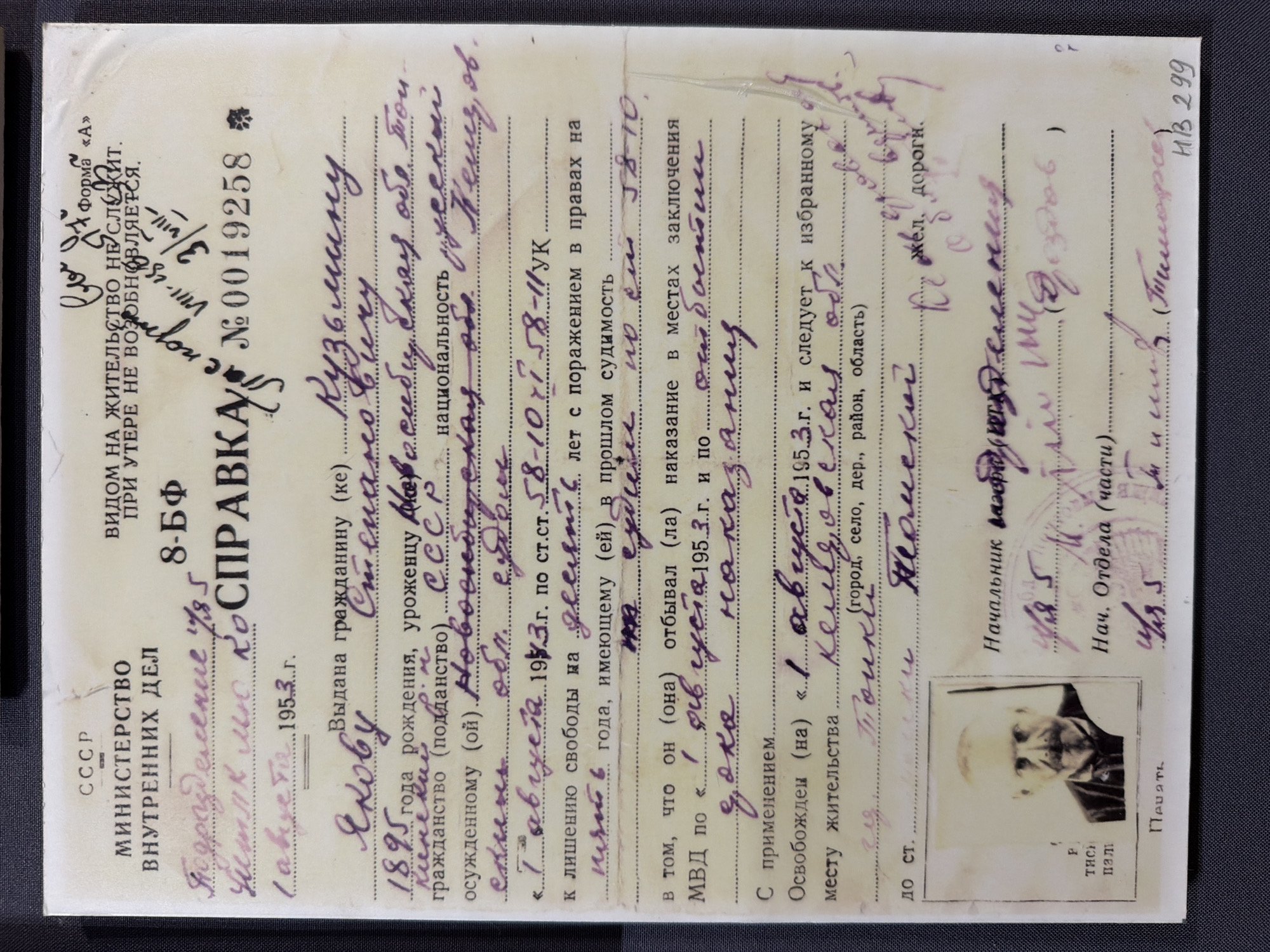 The image is a scan of a Soviet internal passport, likely issued in the 1950s. The document is predominantly text with some handwritten entries. The top section has official stamps and seals, including "CCCP" and "МИНИСТЕРСТВО ВНУТРЕННИХ ДЕЛ". There is a small black and white photograph of an elderly man with a mustache and a goatee, wearing a dark suit and a medal. His left hand is visible, resting on the bottom edge of the frame.
The handwritten text appears to be personal details and legal information related to the passport holder. Some legible entries include: "1895 года рождения", "уроженцу (кой)", "гражданство (подданство) СССР", and information about criminal proceedings and imprisonment. There are also sections for the holder's place of residence and release details.
A key piece of handwritten information is "месту жительства ... kemi, ob." (place of residence ... Kemi, ob.) and "до ст. ... Torcкu ... Toмcku" (to station ... Tocki ... Tomsk). This suggests that the individual was released and possibly relocating to or from the region of Tomsk, Russia. The city of Ust'-Pyzas is not explicitly mentioned in the visible text.