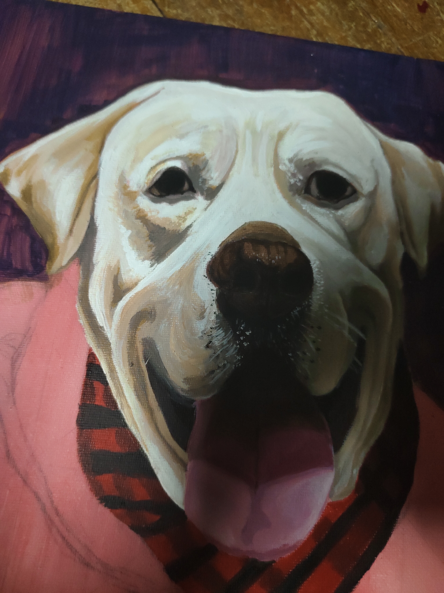 The image presents a close-up painting of a cream-colored dog, likely a Labrador Retriever, rendered with visible brushstrokes on what appears to be a canvas. The dog faces directly towards the viewer with an open-mouthed, smiling expression, its pink tongue extended downwards. Its dark eyes are fixed forward, and the dark brown nose shows a wet, textured appearance. The fur around the muzzle and jowls is depicted with varied tones, indicating highlights and shadows. The dog is wearing a plain pink garment around its neck and chest, underneath which a red and black plaid pattern, resembling a bandana or collar, is visible on the viewer's left side. The background behind the dog is a solid, dark maroon or deep purple. A narrow strip of a light brown, textured surface, possibly wood, is visible along the top edge of the image. This scene is situated in the context of Davao City, Philippines.