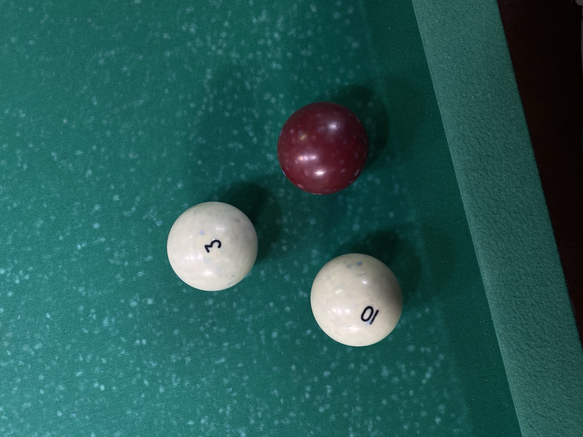 The image shows a close-up of a billiard table with three billiard balls on it. Two of the balls are white with the numbers "3" and "10" printed on them. The third ball is dark red. The billiard table is covered in green felt. The image does not contain any information about the location in the city of Chaikovsky, Russia.