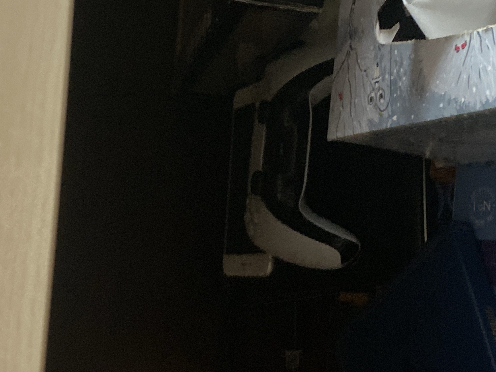The image shows a dimly lit, confined space. A white object with black accents, possibly a shoe or a component of a larger device, is visible near the center. Part of a box with a winter-themed design is present in the upper right. A dark-colored object, possibly a book or box, is situated at the bottom right. The background is a dark, blurry expanse. There is no indication of a location in Sofia, Bulgaria, or any other specific place. There are no people or actions visible in the image.