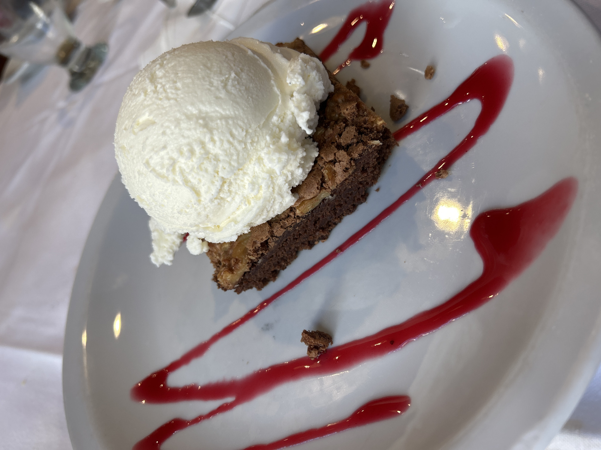 A dessert is presented on a white plate. It consists of a brownie topped with a scoop of vanilla ice cream and a red berry sauce is drizzled artistically around the dessert. The setting appears to be indoors, possibly a restaurant or café. The location is unspecified and the reference to Buenos Aires, Argentina is extraneous.