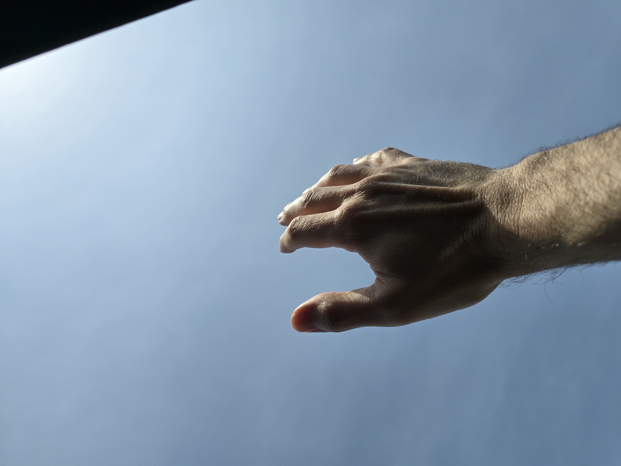 A hand extends into a blue sky. The lower left corner has a dark, blurred object. The location and city are unknown.
