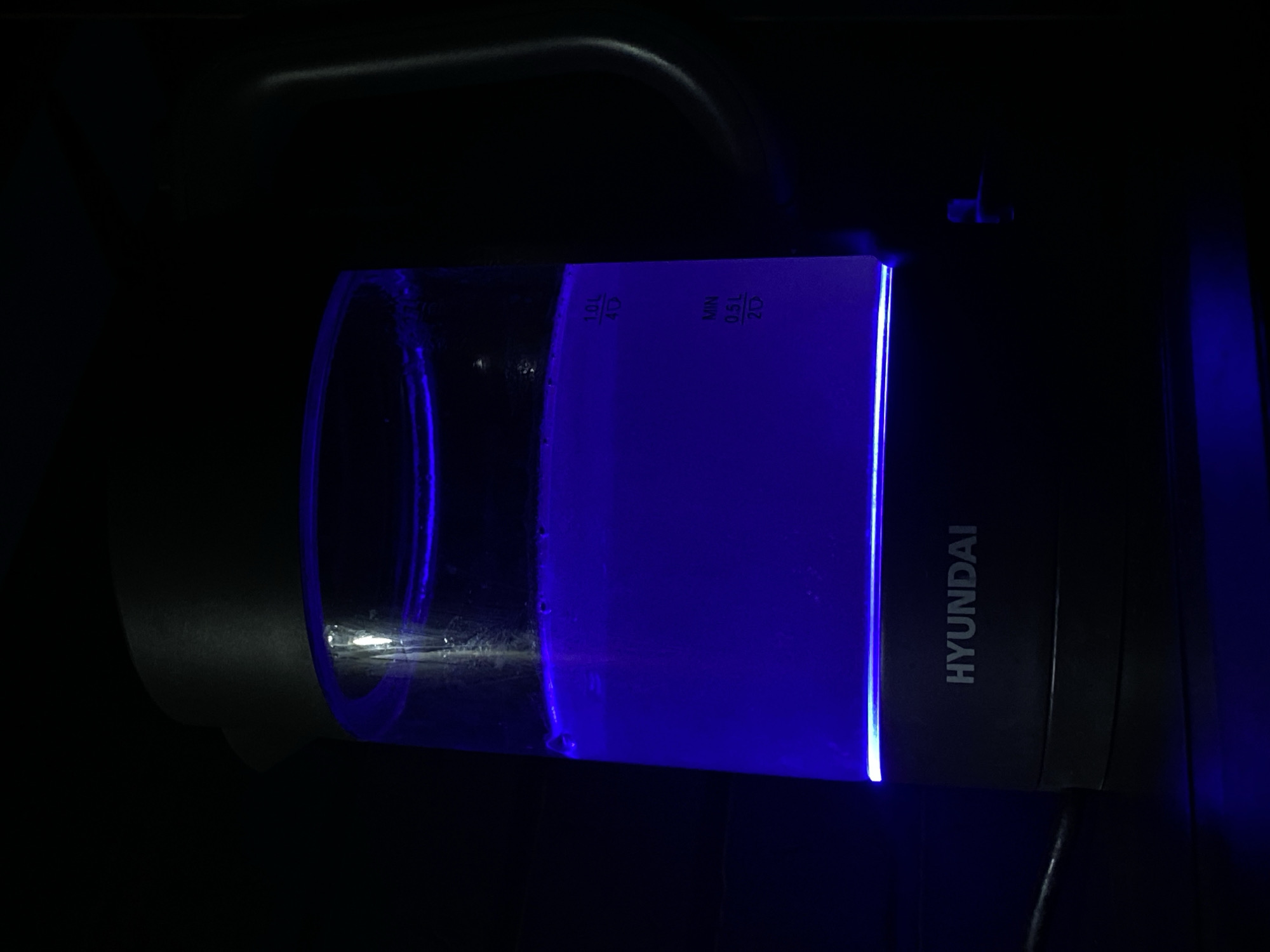 A close-up image depicts a Hyundai electric kettle, illuminated with a blue light. The kettle contains water, filled to approximately the 0.75 L mark on the transparent container. The environment is dark, suggesting an indoor setting. The "HYUNDAI" branding is visible on the kettle's body. Location in Sochi, Russia cannot be determined from the visual information.