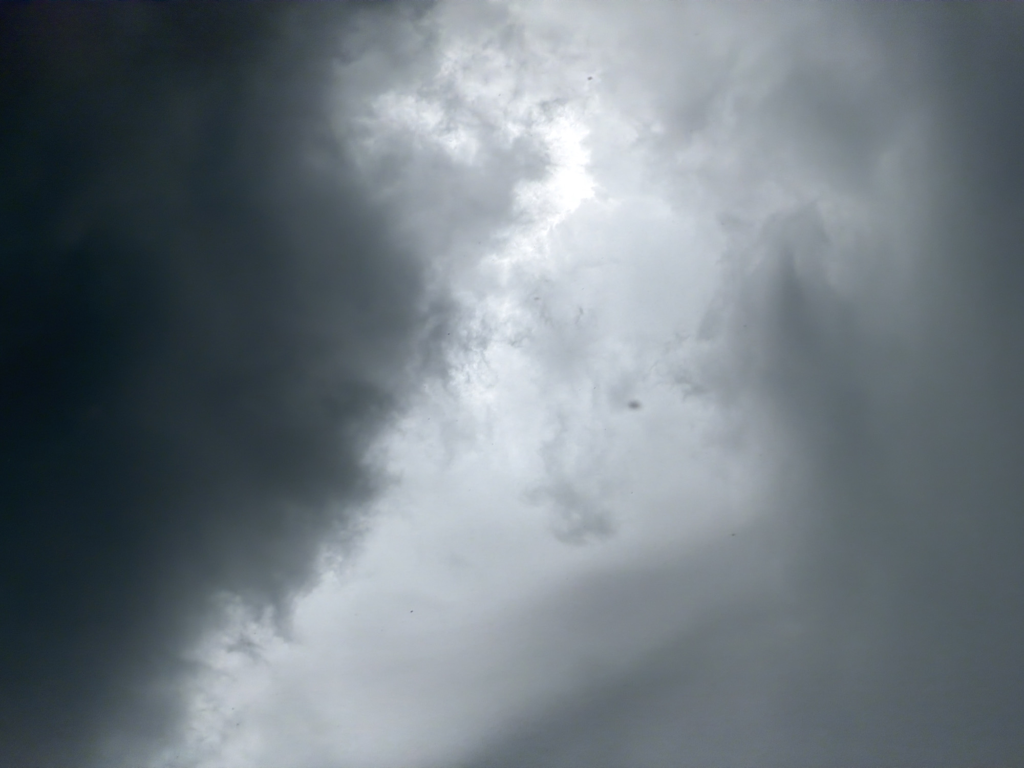 The image shows a view of a stormy sky. The sky is filled with dark, ominous clouds, and a patch of brighter, white sky can be seen in the center. The heavy cloud cover suggests a possible storm or heavy rain. The location cannot be determined from the image, and the presence of people, subjects, objects, actions, and interactions are not visible.