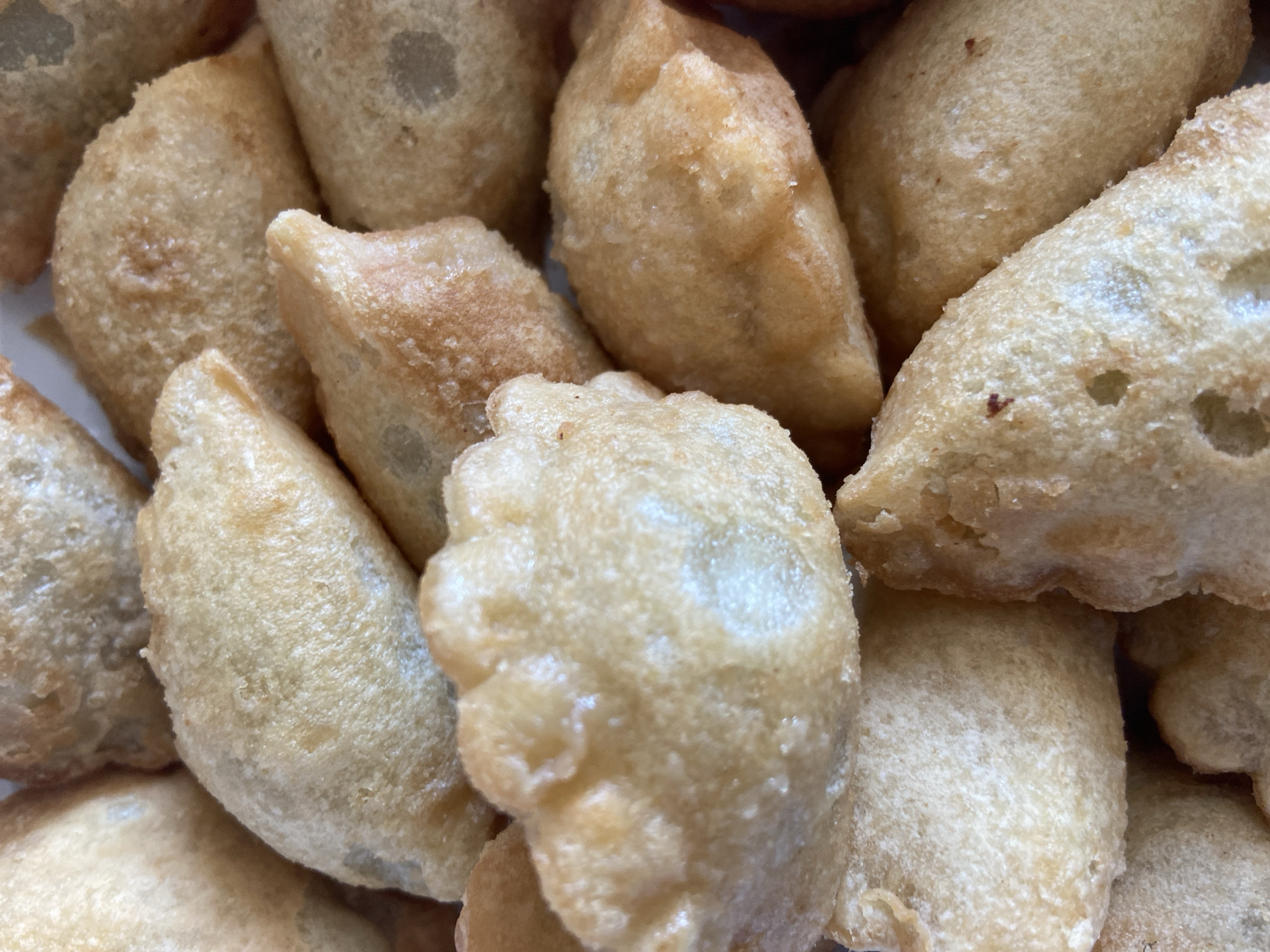This media file is a close-up shot of a pile of fried dumplings, likely pierogi, a traditional dish in Ufa, Russia. The dumplings are golden brown and appear to be freshly cooked, with a slightly crispy texture visible on their surfaces. Some dumplings have a darker, more textured appearance, suggesting they may have been fried for a longer period or contain a filling that has browned. The dumplings are tightly packed together, filling the frame of the image. There is no visible text in the image. The lighting appears to be bright and even, indicating an indoor setting, possibly a kitchen or a serving dish. The focus is sharp on the dumplings, highlighting their texture and shape. The scene evokes a sense of homemade food and comfort, common in domestic settings in Ufa.