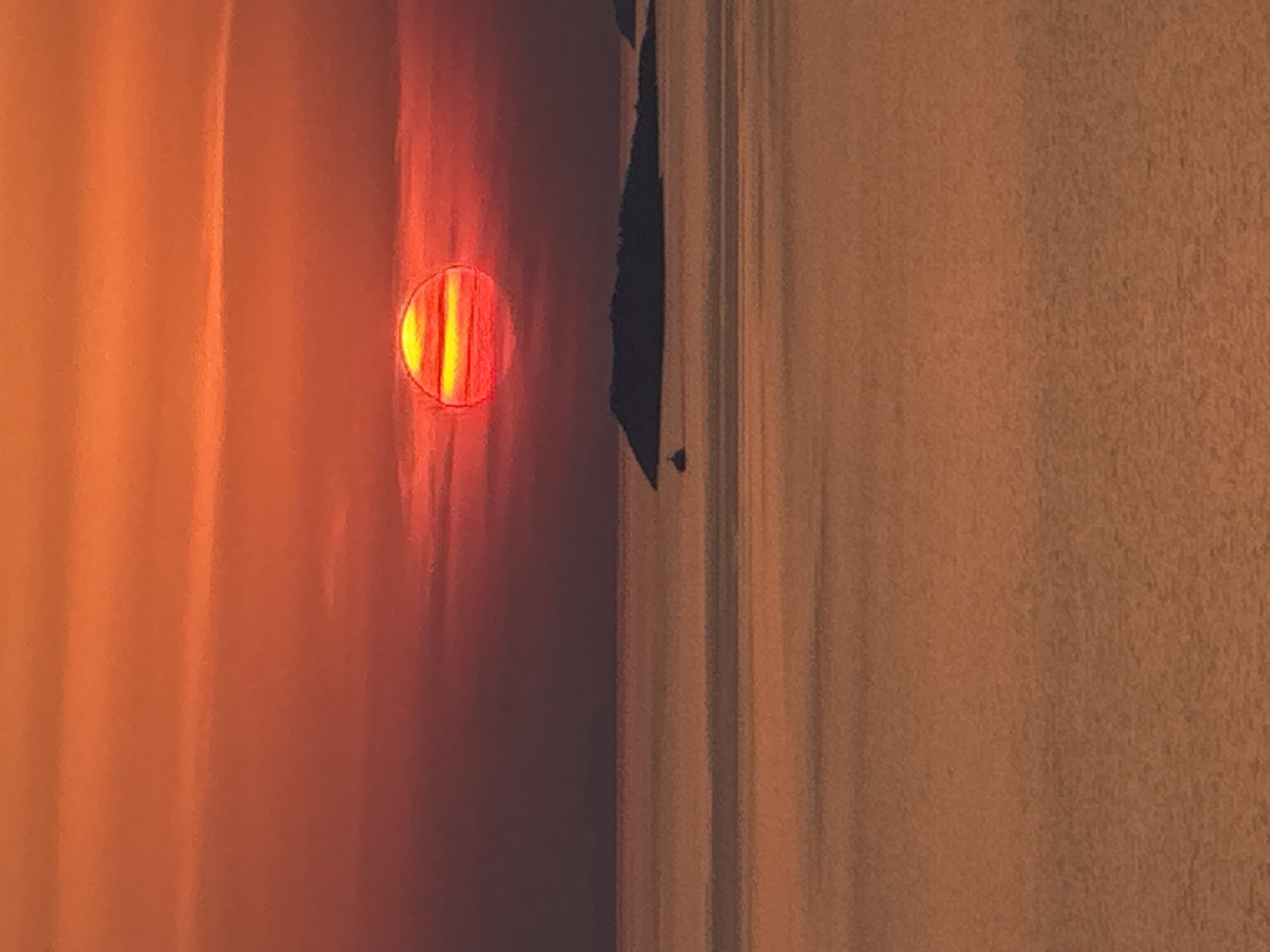The image shows a vibrant sunset over the Adriatic Sea, with the sun a large, reddish-orange orb with horizontal streaks of yellow and red. The sky is filled with bands of orange and red clouds, becoming darker towards the top of the frame. In the distance, the silhouetted forms of islands are visible, with a small boat in the water to the left of the largest island. The sea is a calmer expanse of orange and brown hues, reflecting the colors of the sunset. The scene is set in the vicinity of Zagora, Montenegro, known for its beautiful coastal landscapes.
