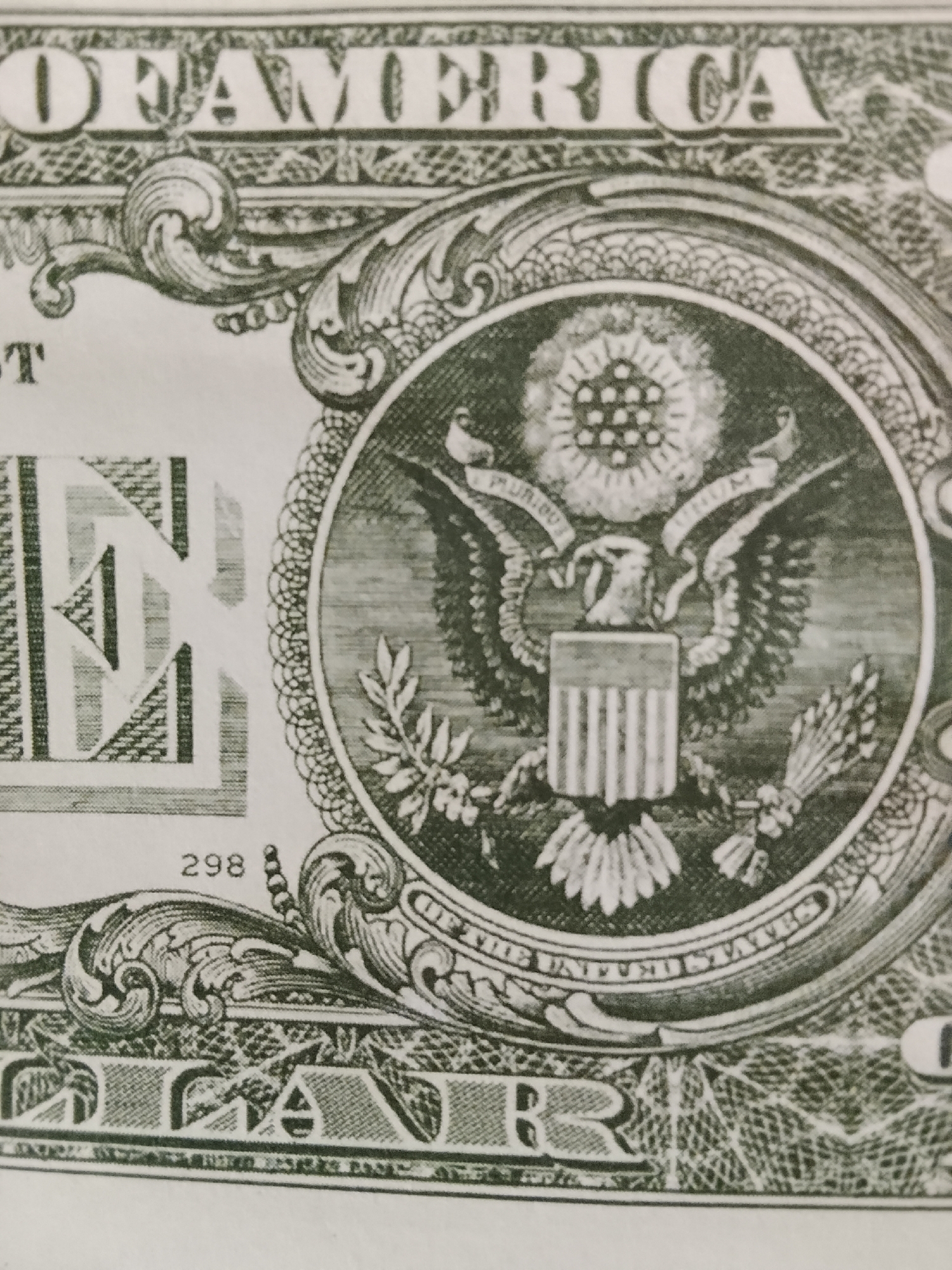 The image shows a close-up of a US one-dollar bill. Prominent features include: the words "OF AMERICA," the letter "E," the number "298," and the Great Seal of the United States, featuring an eagle with a shield on its chest, holding an olive branch and arrows, surrounded by the words "E PLURIBUS UNUM" and "THE UNITED STATES."
The location in Multan, Pakistan, is irrelevant. The picture is an object and the location is not relevant to its forensic analysis.