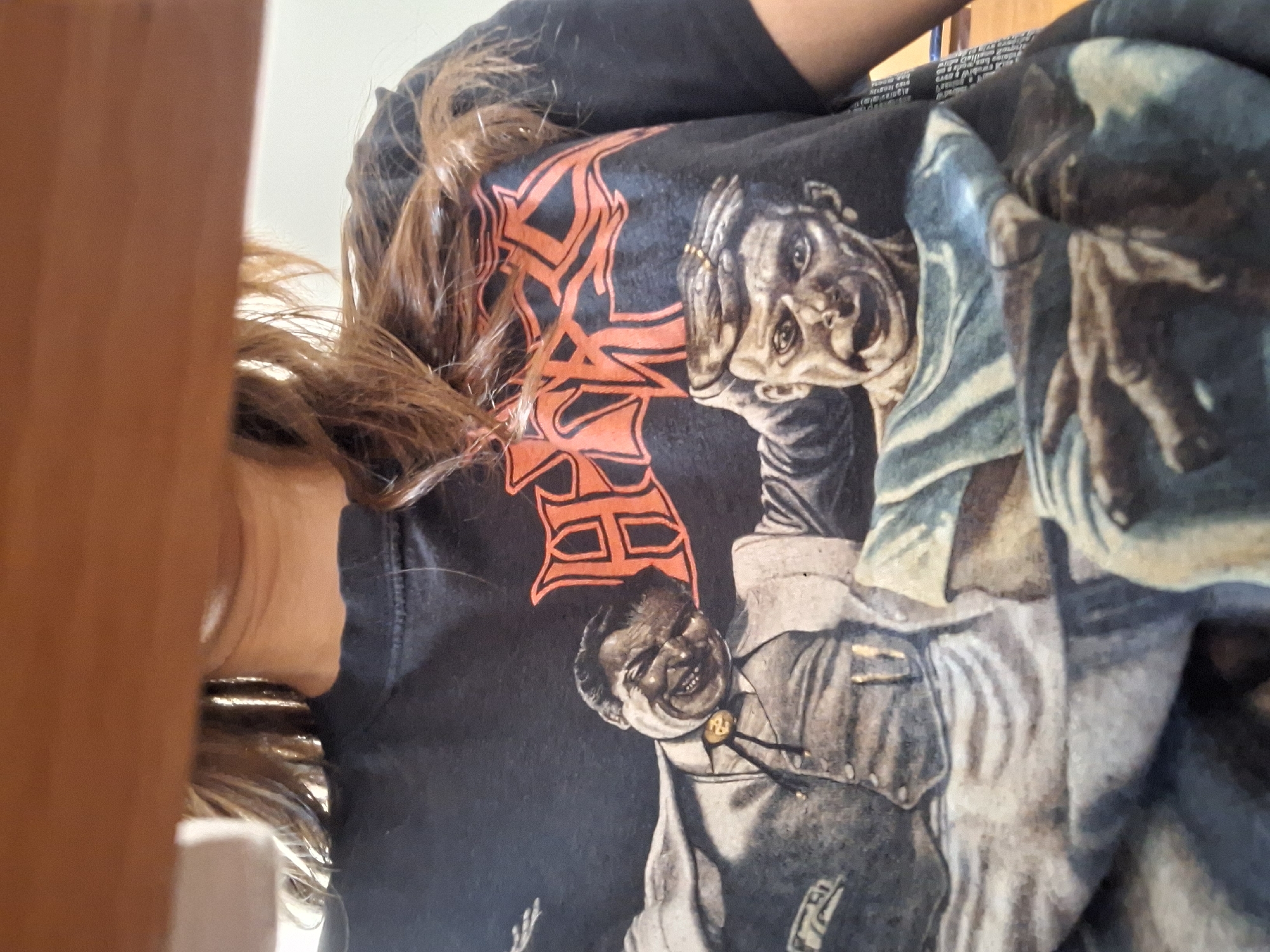 The image shows a person wearing a black t-shirt with a red design and a grayscale image printed on it. The design is partially obscured by the person's hair. The grayscale image features portraits of two men. The shirt has a textured appearance. The location in the city of Panagyurishte, Bulgaria, is not discernible from the visual information provided.