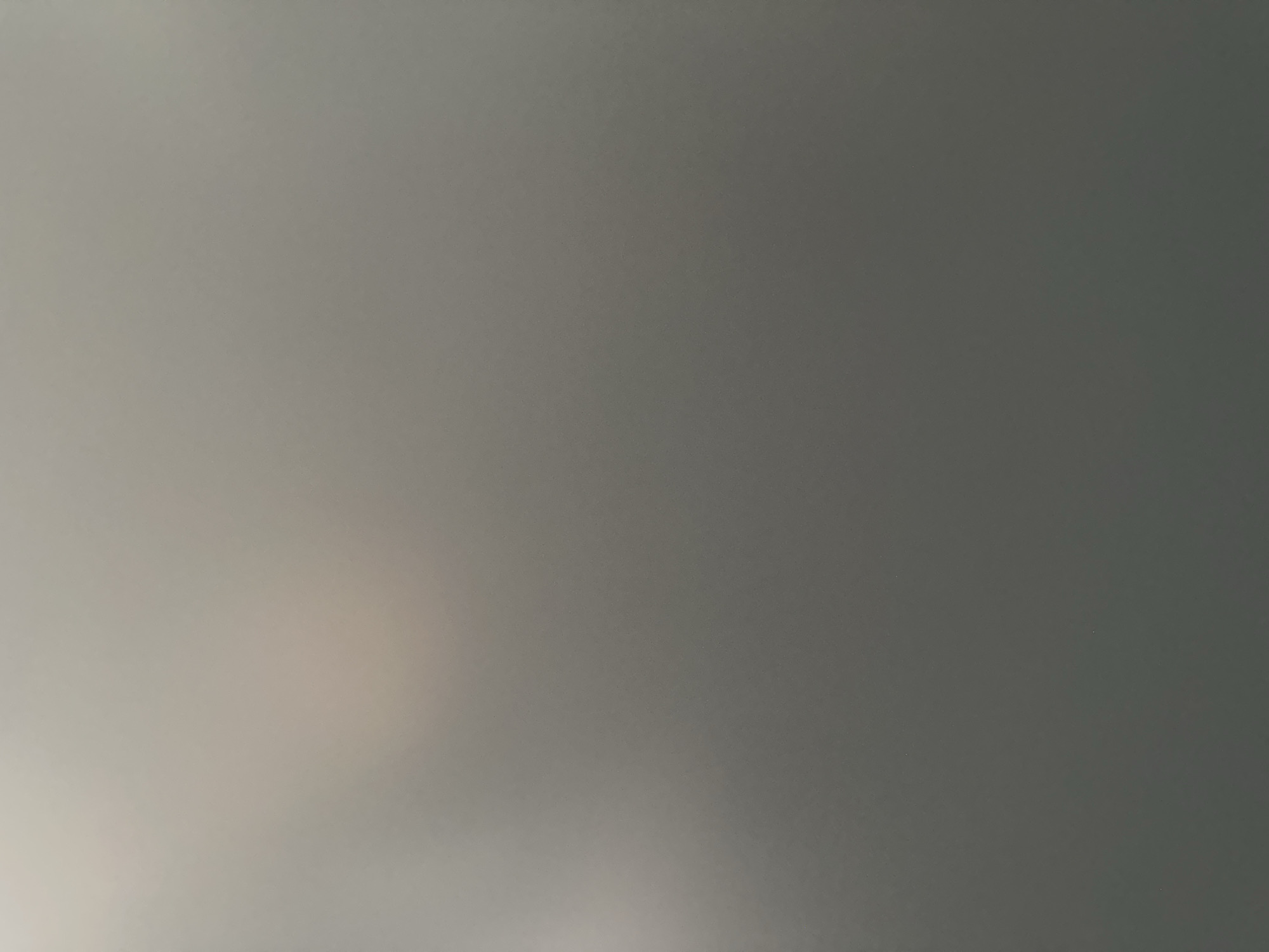 The image is an abstract, out-of-focus shot with a predominantly gray and white gradient. The lighting is soft and diffused, with a bright, washed-out area in the bottom left corner transitioning to a darker, more muted gray towards the top right. There are no discernible subjects, objects, or scenes. The lack of detail suggests it could be a macro shot of a texture, a heavily blurred photograph, or a digital representation of a gradient. No text is visible. The context of Belgrade, Serbia, and any specific time of day, weather, or emotional cues are not inferable from the visual information provided.