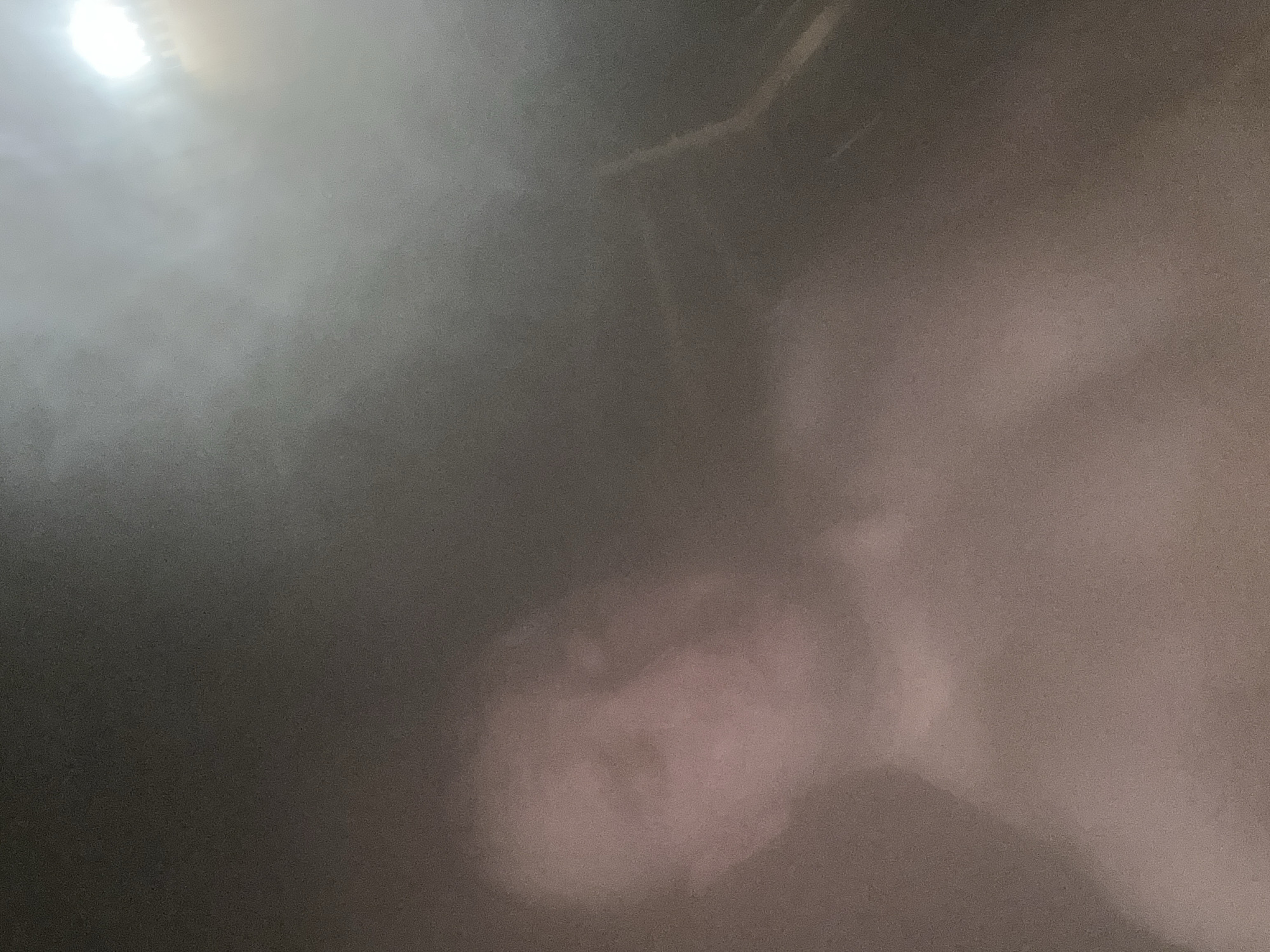 The image is dark and blurry. There is a light source in the upper left. A vaguely human face is discernible in the lower center. The surrounding environment is indistinct. It is not possible to determine the location in Chaikovsky, Russia, or any actions or interactions.