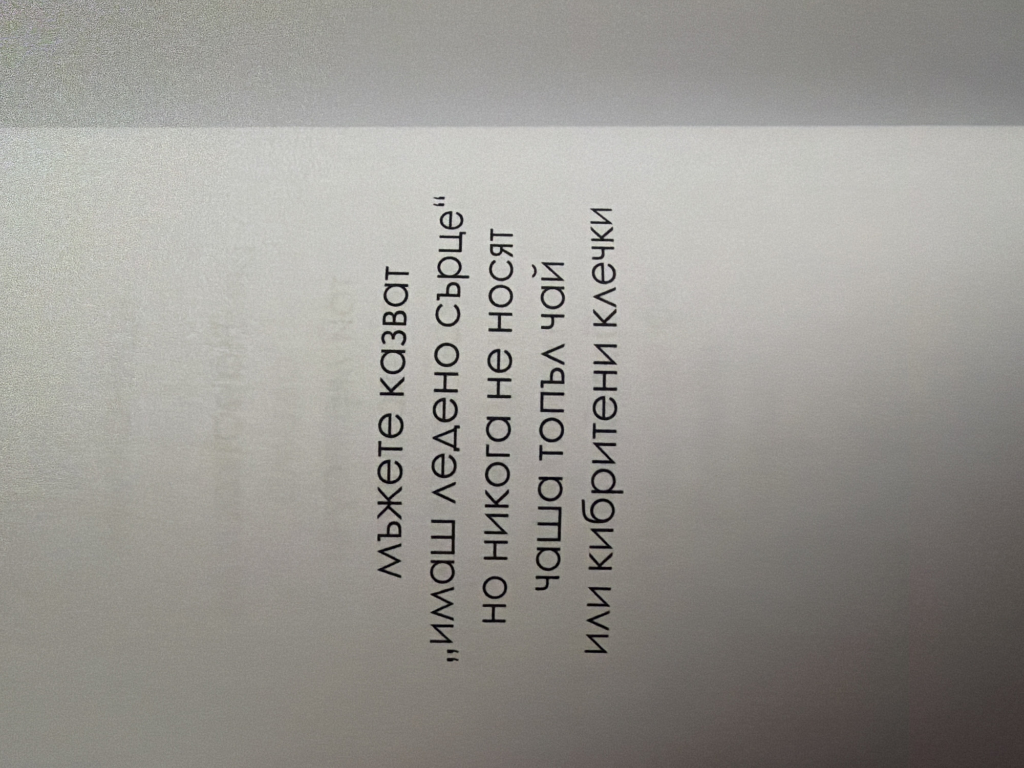 The image displays a white page with black text. The text is in Bulgarian and appears to be a poem or a quote. The text reads:
"мъжете казват
„имаш ледено сърце“
но никога не носят
чаша топъл чай
или кибритени клечки"
This translates to:
"Men say
'You have an ice heart'
but they never carry
a cup of hot tea
or matchsticks"
There are no people, subjects, objects, actions, or interactions visible in the image. The environment is a plain white surface, likely a page in a book or a printed document. The image is a close-up shot of the text, with no discernible elements of the city of Pazardzhik, Bulgaria, or any other specific location.