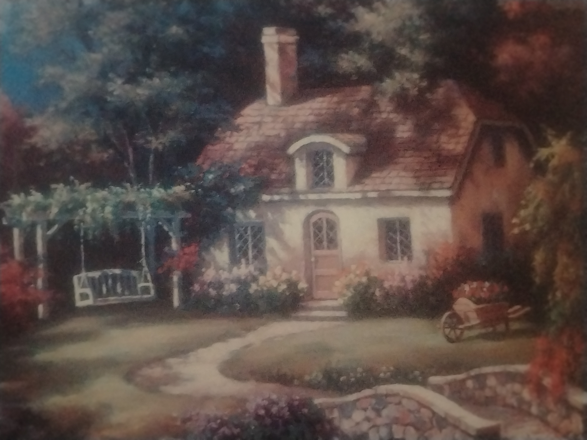 This is a painting of a quaint cottage with a red-tiled roof, nestled within a lush, green garden. A stone path winds through the garden, leading to the cottage's entrance. In the foreground, a stone bridge arches over a small stream. To the left of the cottage, a white swing set hangs from an arbor draped with vines. A wheelbarrow filled with flowers sits to the right of the cottage. The overall impression is one of rustic charm and tranquility. The painting does not depict a specific location in La Tagua, Venezuela, or any specific people or actions.