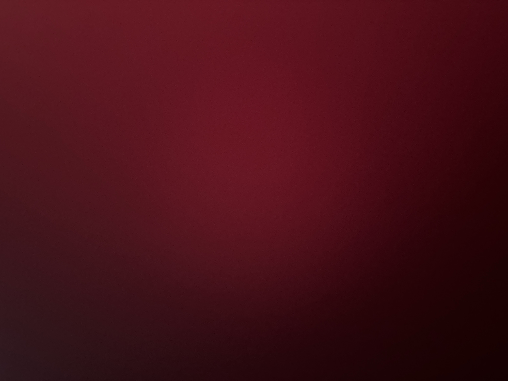 This is a digitally generated image that serves as a background. The dominant color is a deep, rich maroon, transitioning to a darker, almost black shade in the lower left and right corners, creating a subtle gradient effect. The texture appears slightly grainy or speckled, suggesting a matte finish or a low-resolution digital texture. There are no discernible subjects such as people, objects, or scenes. The image does not depict any specific activity or event. There are no visible text elements. The lighting appears diffused and even across most of the image, with the darker tones hinting at a shadow or a fading light effect. Given the absence of any specific visual cues, it is impossible to determine the time of day, weather conditions, or a precise location. The overall impression is one of abstract color and texture, suitable for a minimalistic background.