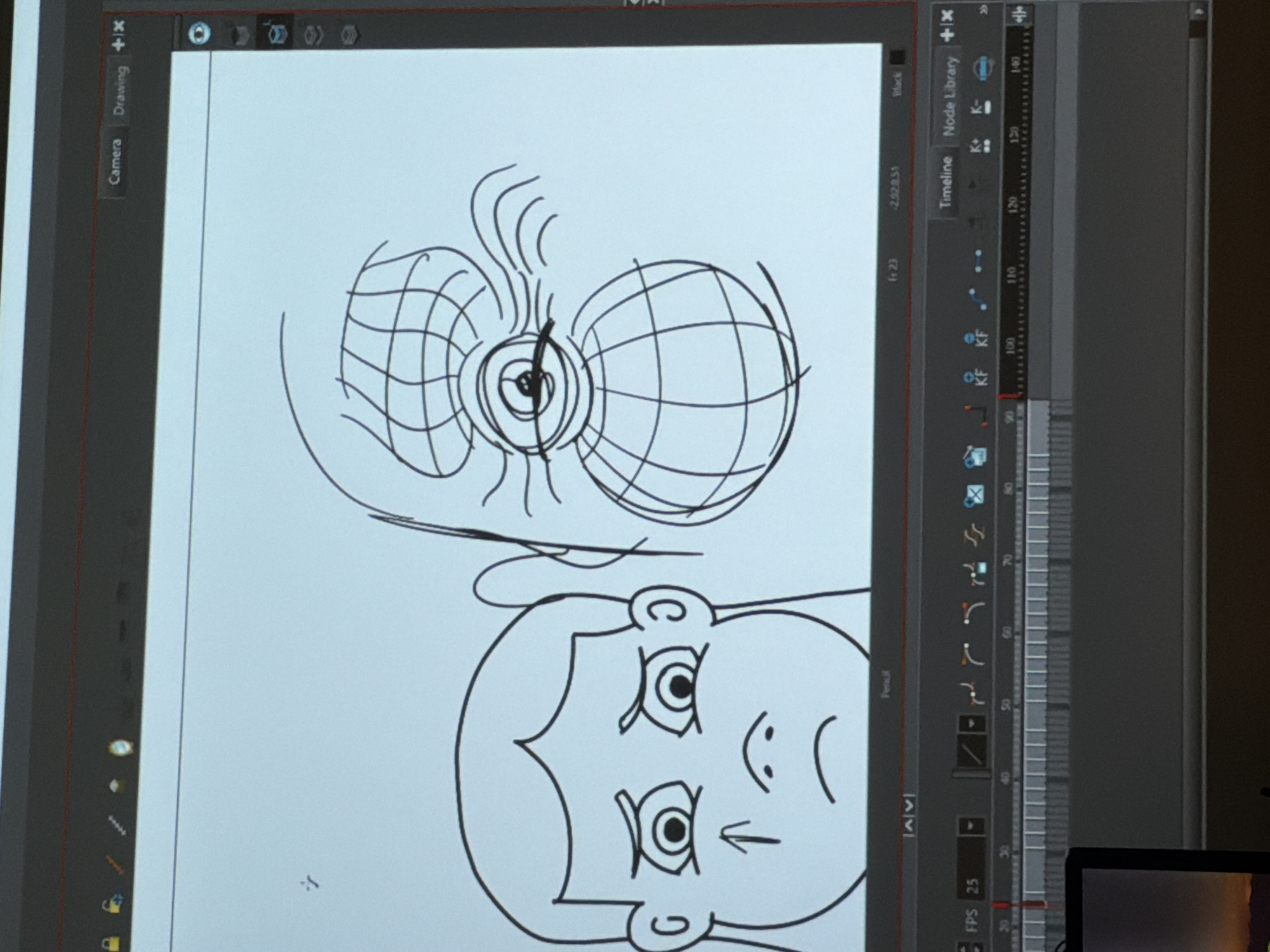 A close-up shot of a computer screen displays animation software. The screen shows a cartoon drawing of a person's face below two spherical objects with intersecting lines and some emanating lines. A timeline and various animation tools are visible on the right side of the screen. The software appears to be set to 25 frames per second (FPS). The location is not identifiable.