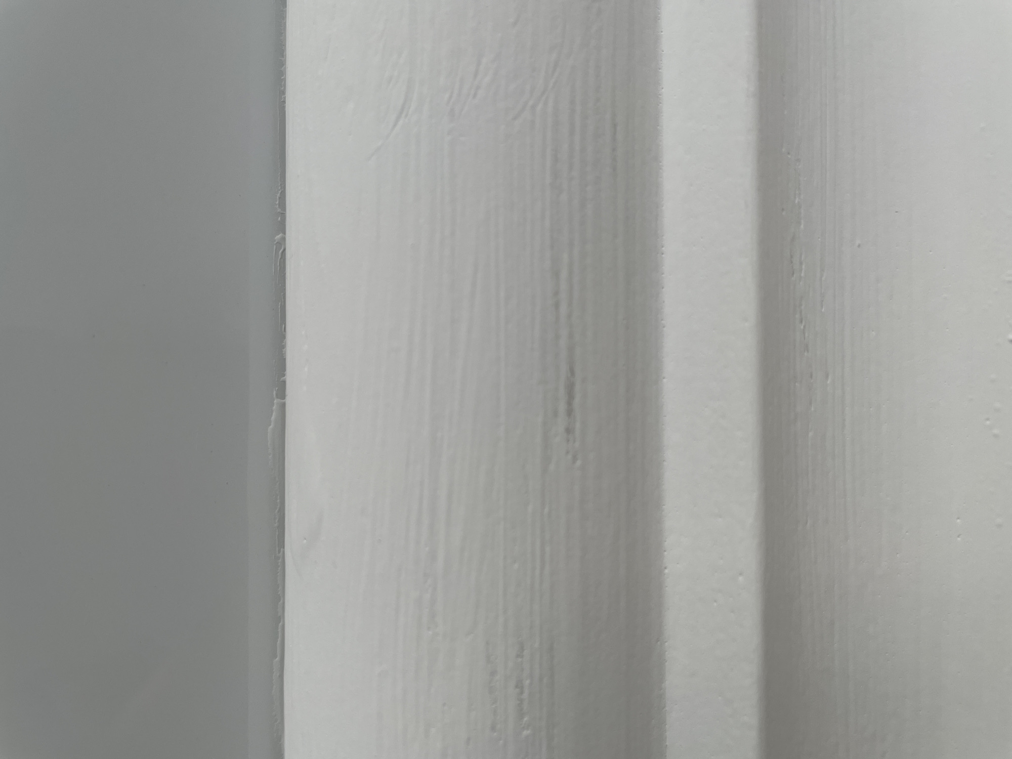The image shows a close-up, abstract view of a white, textured surface with horizontal lines. The surface appears to be a wall or a similar architectural element, possibly painted wood or textured plaster. There is a subtle gradient in the background, transitioning from a lighter gray at the top to white at the bottom. The textured surface itself is predominantly white with some areas of light gray shadowing and subtle imperfections or variations in the texture. There are no people, objects, or discernible actions in the image. The image does not contain any information that would allow for its location to be identified as Omsk, Russia.