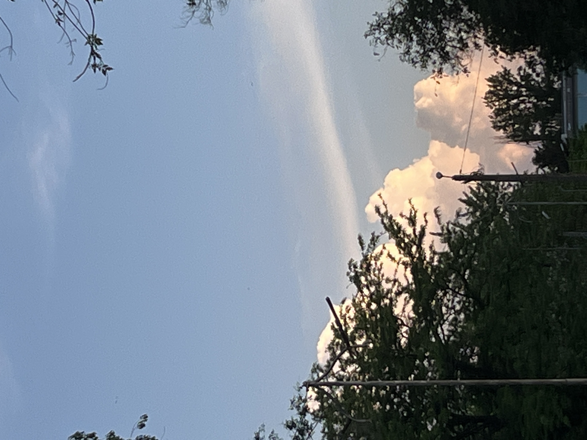 The image depicts a view of the sky with scattered clouds, partially obscured by tree branches. A utility pole with wires is visible against the backdrop of a large cloud formation. The location is identifiable as Shyroka Dacha, Ukraine, based on provided information. No people or actions are visible in the image. The environment consists of natural elements (sky, clouds, trees) and man-made infrastructure (utility pole).