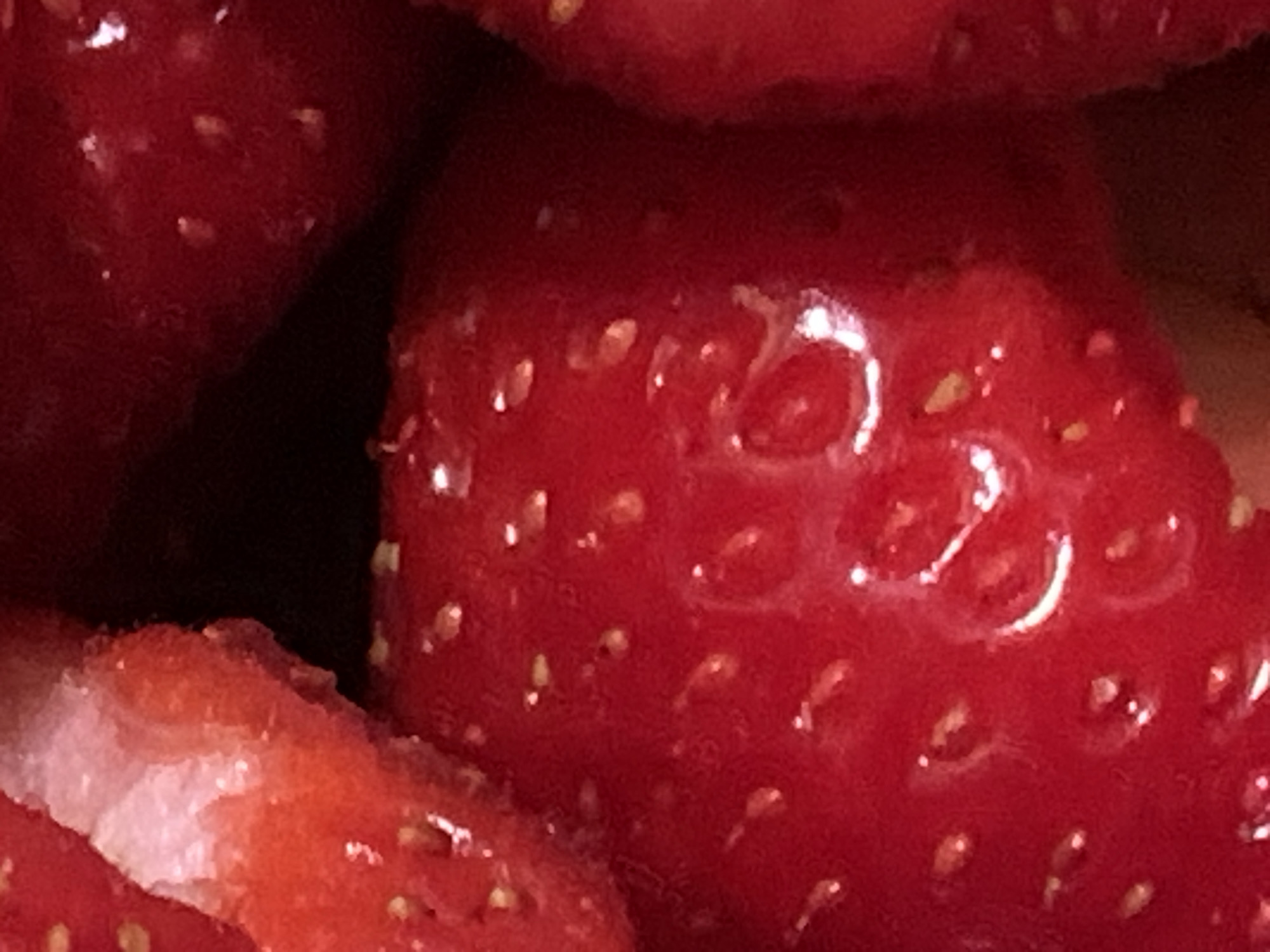 A close-up image depicts a group of strawberries, characterized by their red coloration and small, yellowish seeds embedded in the surface. One strawberry appears to be cut, revealing a lighter, white interior. The overall composition is tightly framed, concentrating on the texture and detail of the fruit. The location is Unknown, Unknown.
