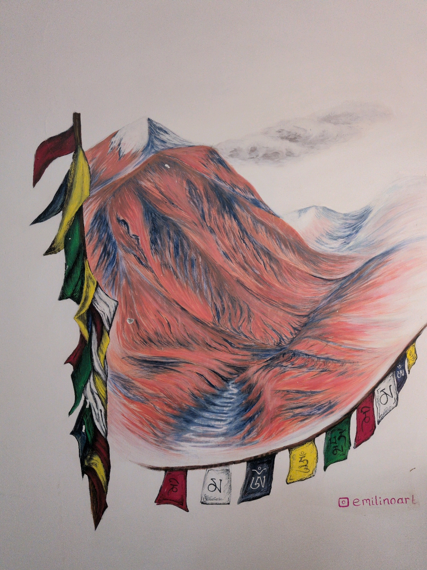 The image depicts a drawing of prayer flags strung across a mountainous landscape, likely inspired by the region of Leh, India. The flags, in various colors including red, yellow, green, blue, and white, are rendered with intricate details, some bearing symbols. The mountainous terrain is characterized by dramatic peaks, with one prominent peak colored in shades of red and blue, suggesting ruggedness and altitude. Snow-capped summits and wisps of clouds add to the atmospheric quality of the scene. The artwork is signed "emilinoart" in the lower right corner.