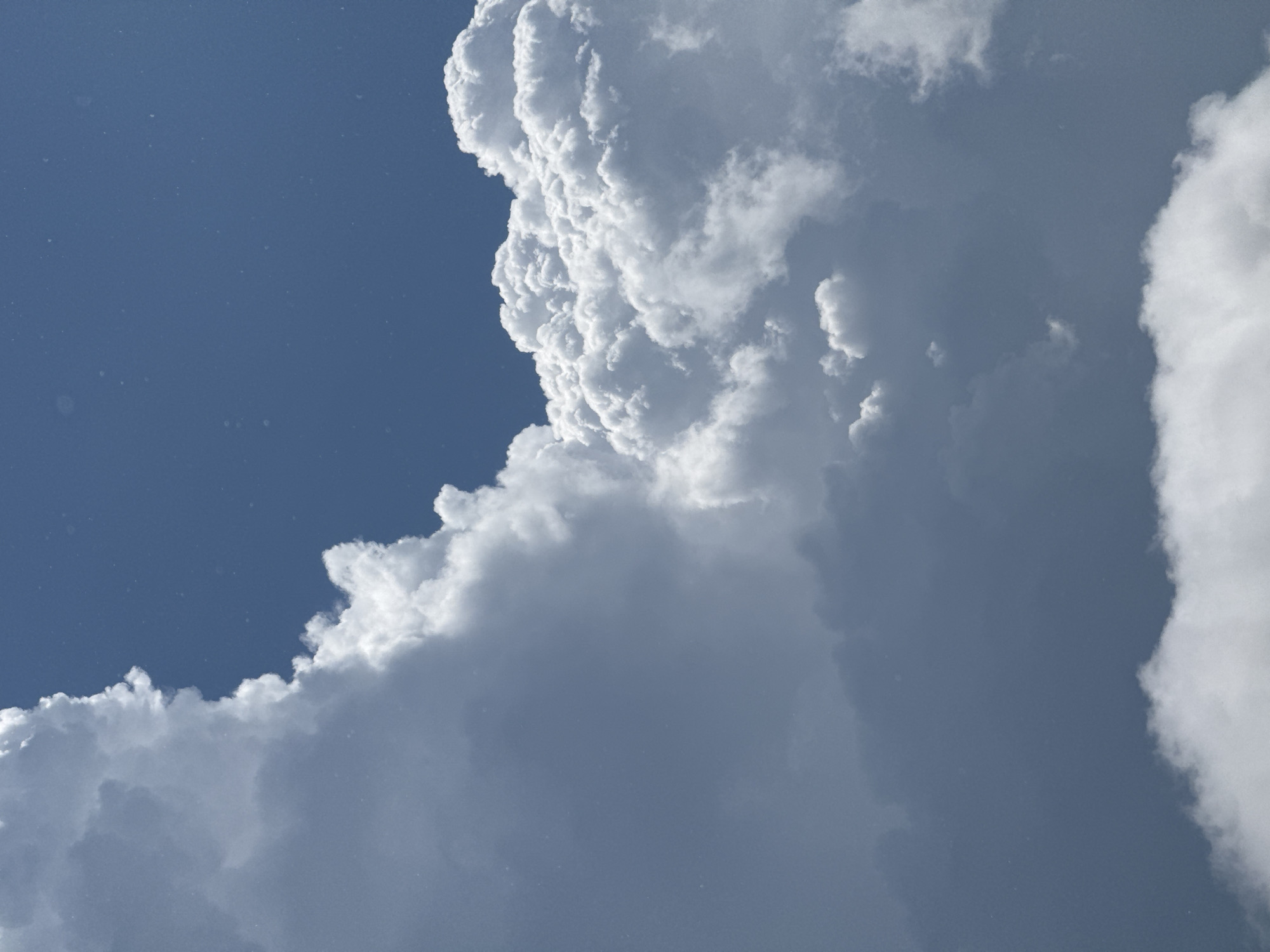 The image shows a portion of the sky with white and gray clouds against a bright blue sky. There are no people or man-made objects visible. The location is given as Mikhaylovsk, Russia, suggesting this is an outdoor scene.