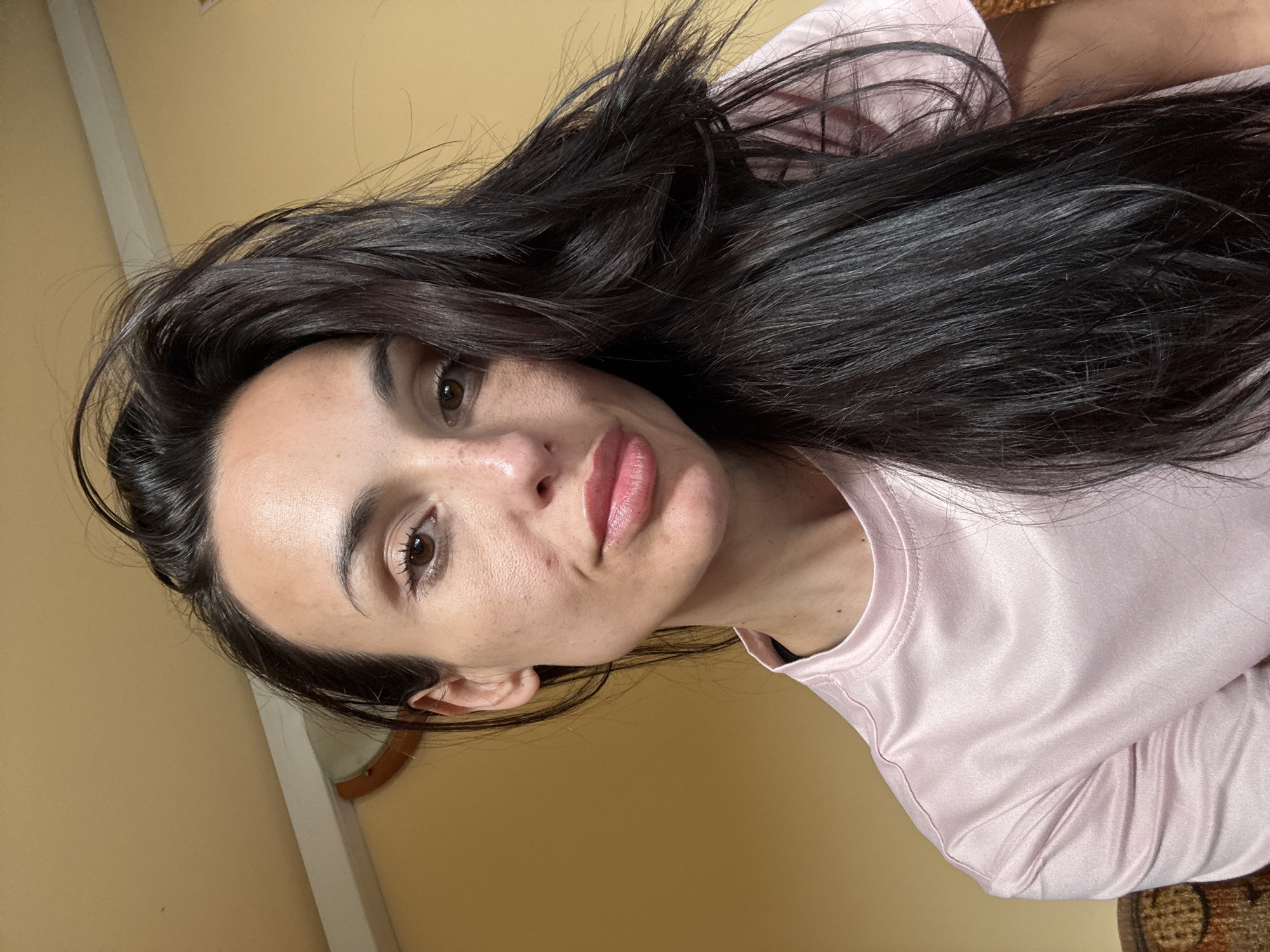A woman with dark hair is facing the camera. She's wearing a light pink shirt. The background is a plain yellow wall. There is no evidence to suggest the location is Pleven, Bulgaria.