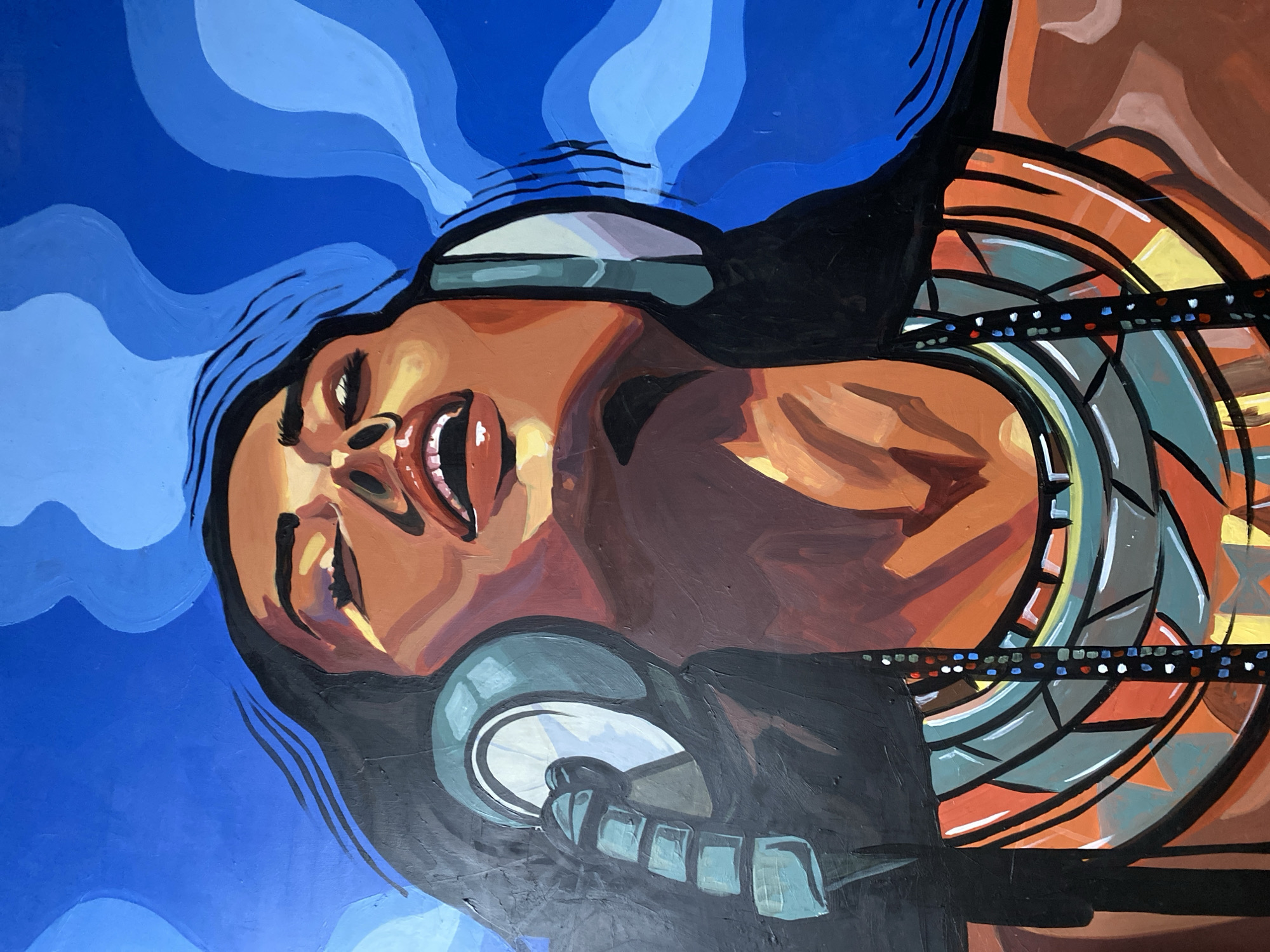 This is a painting of a woman wearing headphones and a necklace, with her head tilted back. The background is a vibrant blue with wavy lines, suggesting movement or sound. The woman's eyes are closed, and her mouth is open, as if she is deeply engrossed in the music. She has long black hair that appears to be blowing in the wind. Her skin tone is warm, and she is wearing a colorful, geometric necklace. The painting style is bold and expressive, with thick brushstrokes and strong contrasts. The location of this artwork in Howayi, Nigeria, is unknown as the image itself does not provide any contextual information about its specific placement within the city.