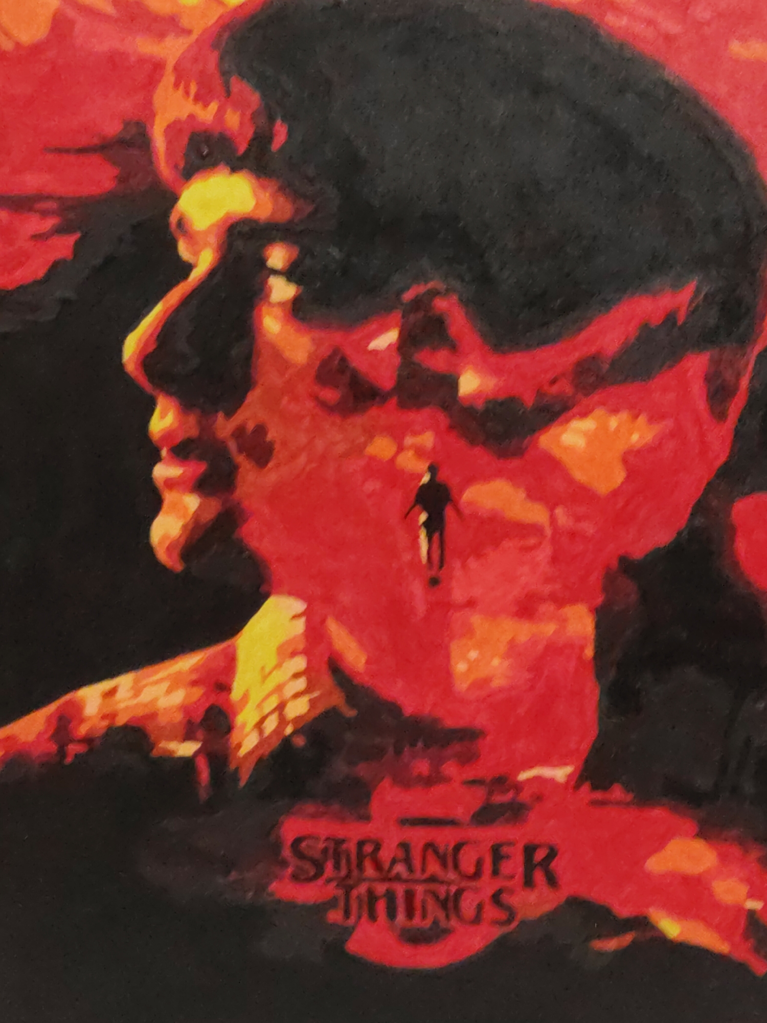 The image is a painting of a profile of a person's head in red and orange tones, with the person's hair colored in black. The name of the TV show "Stranger Things" is at the bottom. Inside the person's face is a dark silhouette of a figure standing in a red landscape. The overall tone is dark and mysterious.