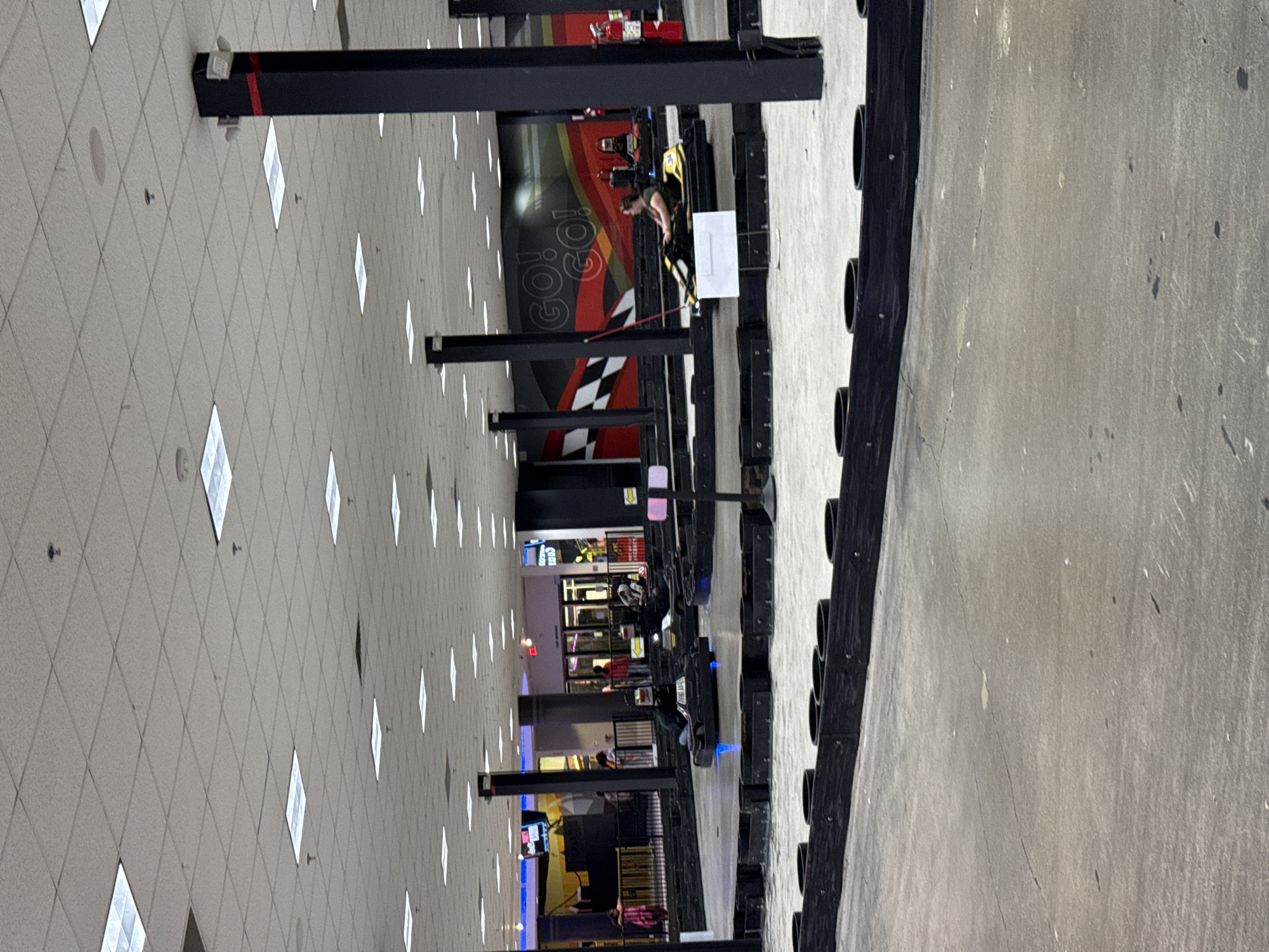 The image shows an indoor go-kart racing facility located in Columbus, Ohio, United States. The go-kart track is visible with karts and riders present. The interior features a drop ceiling with recessed lighting and support columns throughout. There are also sections of the facility with additional entertainment options.