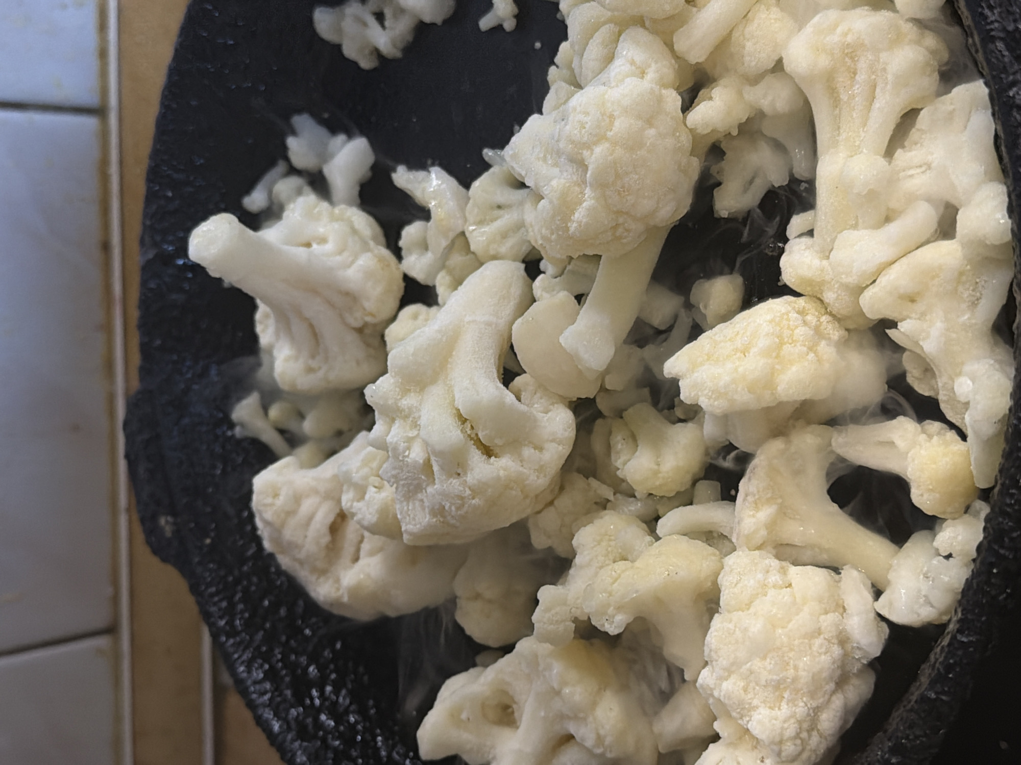 A close-up shot depicts a black pot filled with raw, white cauliflower florets. Some of the florets appear to be slightly frosted. The scene is indoors, with a tiled wall visible in the background to the left of the pot. No people or specific actions are evident. No information is available in this image to confirm its location in Perm, Russia.