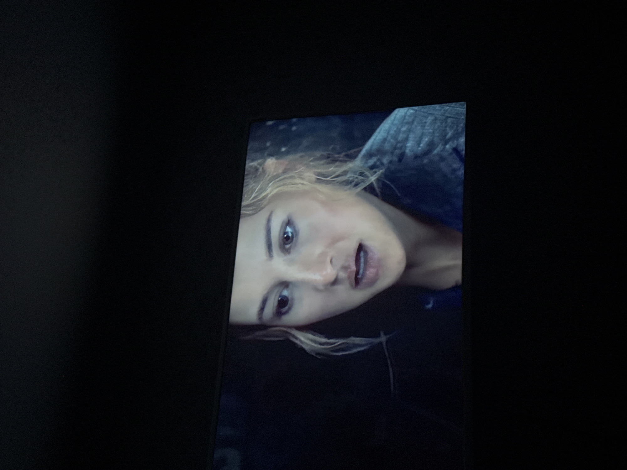 The image shows a close-up of a woman's face on a screen. The woman has fair skin, blonde hair, and is wearing a blue garment. The background is dark. The location is not discernible from the image and therefore cannot be identified as Mytishchi, Russia.