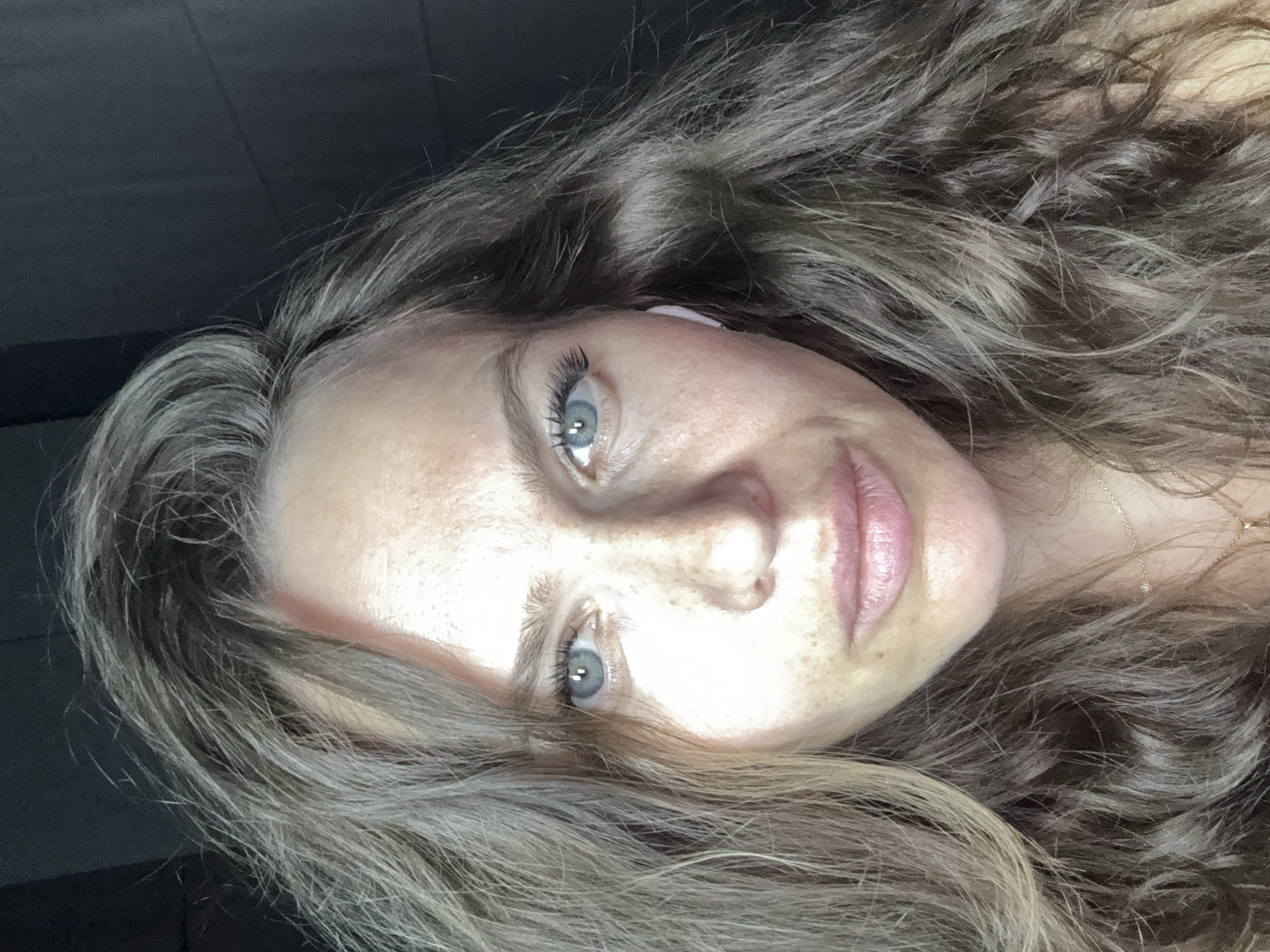 A selfie of a woman with wavy, long brown hair, light skin, and blue eyes. She has freckles on her face. She appears to be indoors. There are no indications to prove it was taken in Khimki, Russia.