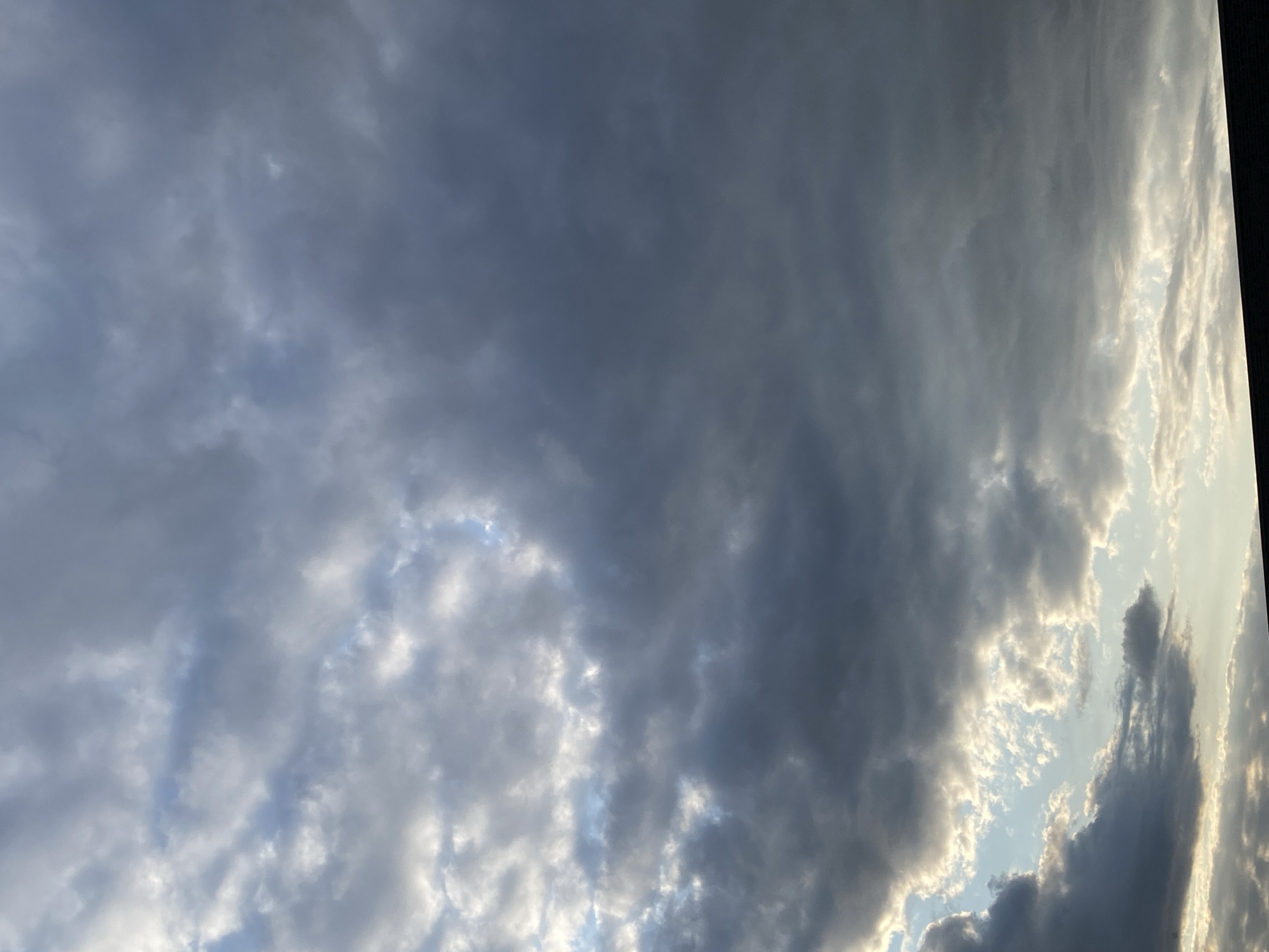 The image shows a cloudy sky over Rinteln, Germany. The clouds are dark and heavy, with patches of light breaking through in some areas. The sky is a mix of grey and blue. In the lower part of the image, there is a dark horizontal line which could be the silhouette of a building or a roof. There are no people or discernible objects in the sky.