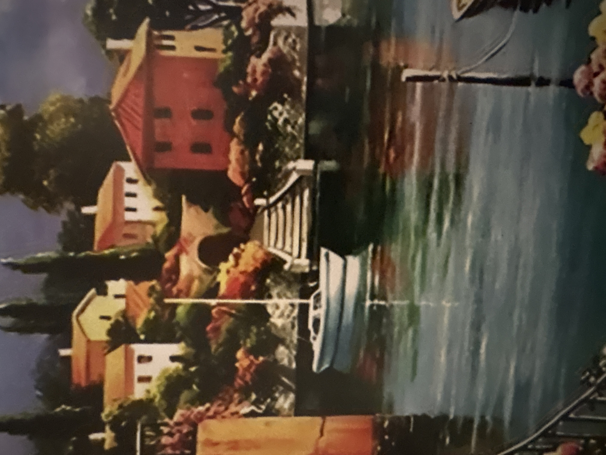 The image depicts a painting of a waterfront scene with buildings and boats. In the background, there are multiple buildings of various sizes and colors (red, yellow, white) nestled amidst greenery. A stairway leads down to the water. A small white boat is visible in the water near the dock, reflecting the scene above. The water appears calm with visible reflections. The foreground of the water exhibits dark and murky tones.
The painting does not depict Plovdiv, Bulgaria.