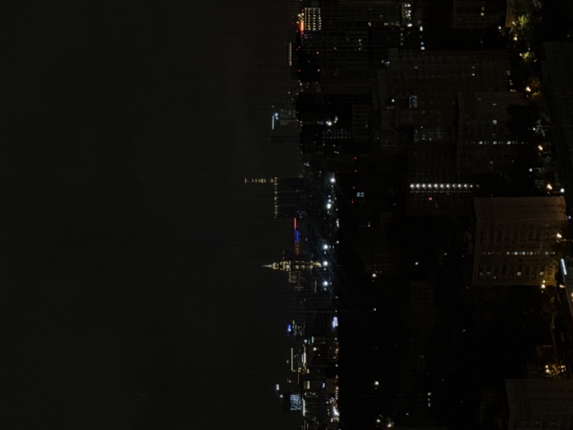 The image depicts a nighttime urban landscape, possibly a city skyline. Structures with illuminated windows and streetlights suggest a built environment. The absence of daylight and the presence of artificial lighting indicate it is after dark. The city is unidentified, and there is no verifiable connection to Khimki, Russia, based on the visual evidence. The image lacks discernible people, interactions, or actions. The environment is dark with scattered light sources.