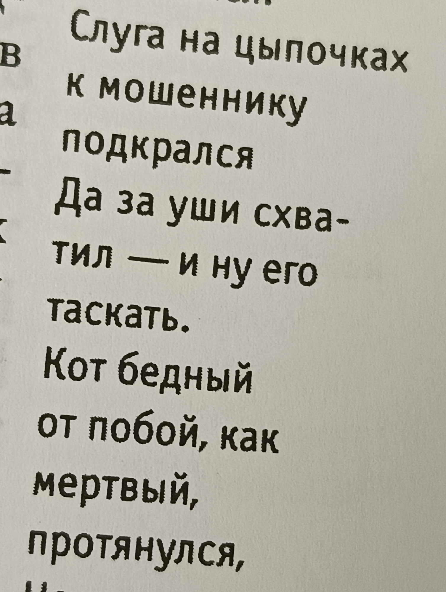 The image shows a close-up of a printed text in Russian. The text appears to be a poem or a story, with multiple lines of text arranged vertically. The font is dark and bold, with some texture suggesting it might be printed on textured paper. The text is in focus, and the background is blurred and plain white, indicating the image was taken from a close distance. There are no people, objects, or environmental details present in the image, other than the printed text itself. There is no indication of a specific location or city.