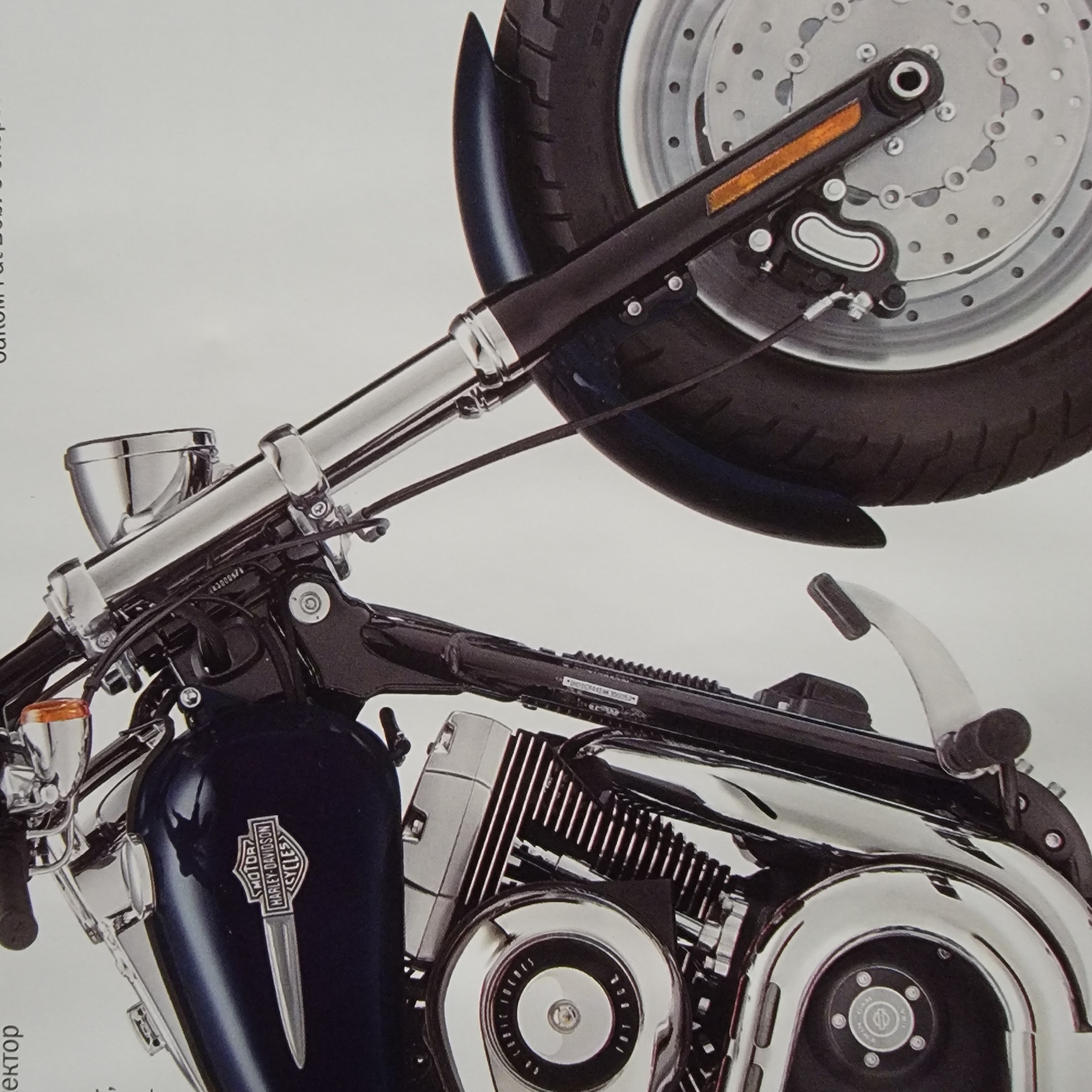 A close-up, head-on view of the front half of a dark blue Harley-Davidson motorcycle is shown against a plain white background. The motorcycle is stationary. The visible components include the front tire and wheel with a disc brake, the front fork, the handlebars, the headlight, and the fuel tank with the Harley-Davidson logo. The motorcycle's engine, a chrome and black V-twin, is also prominently displayed. The lighting is even, suggesting an indoor studio setting or an overcast day. There are no people or other objects visible in the frame.