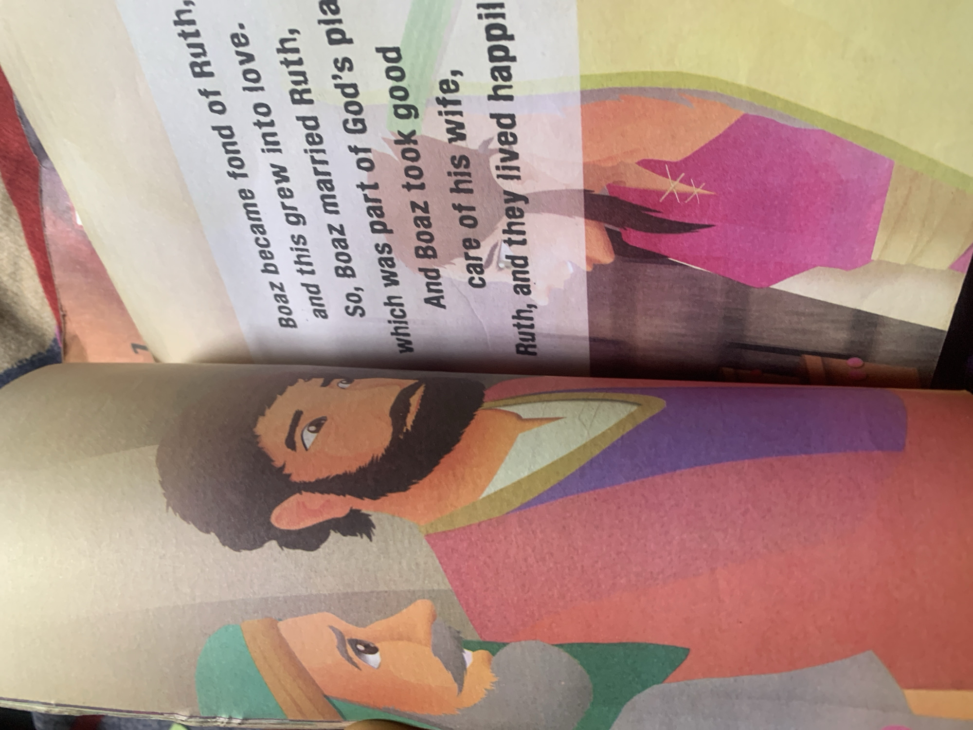 The image shows an open book with illustrations and text. On the left page, there are illustrations of three male figures. The first figure on the left wears a teal headdress with a tan band and has a tan face with a mustache. The second figure is in the center, with dark hair and beard, and is wearing a reddish-pink garment over a white and purple tunic. The third figure is partially visible on the far right. The right page contains text printed in black, accompanied by an illustration of a female figure with dark hair wearing a bright pink garment with decorative stitching. The text describes a story about Boaz and Ruth. There is no information in the image to suggest a location in the city of Jauro Yinu, Nigeria.