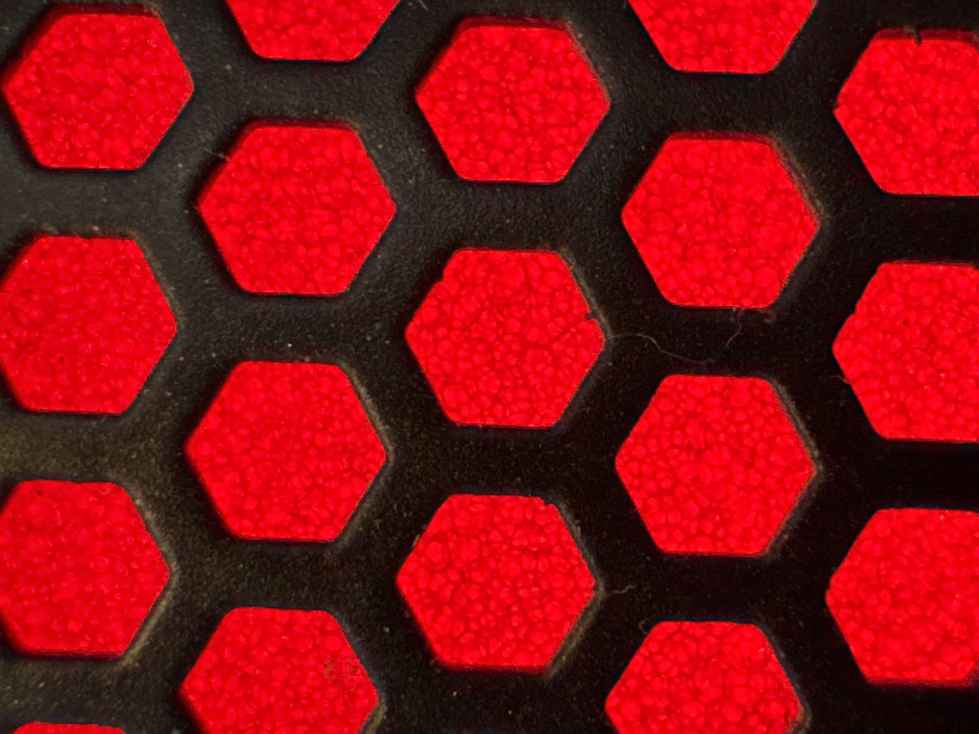 The image shows a close-up of a patterned surface composed of red hexagonal shapes set against a dark, possibly black, background. The red areas appear textured or granular. The pattern appears to be repetitive and organized, suggesting a manufactured or designed surface. There is no information to indicate a location in Burgas, Bulgaria.