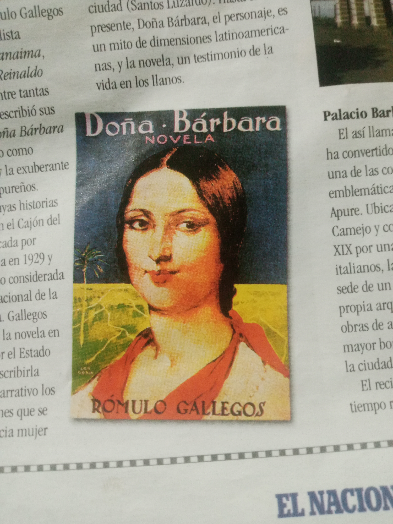 The image is a close-up shot of a newspaper article featuring a book cover titled "Doña Bárbara" by Rómulo Gallegos. The book cover depicts a portrait of a woman with dark hair and red clothing against a background of a palm tree and a field. Text surrounding the book cover discusses the novel and its significance, mentioning its publication in 1929 and its portrayal of life in the Venezuelan plains. It also refers to the "Palacio Barb" and its connection to the city of Apure. The newspaper page itself has a tiled border at the bottom with the text "EL NACION" visible. The lighting is somewhat dim, with the focus primarily on the book cover and surrounding text.