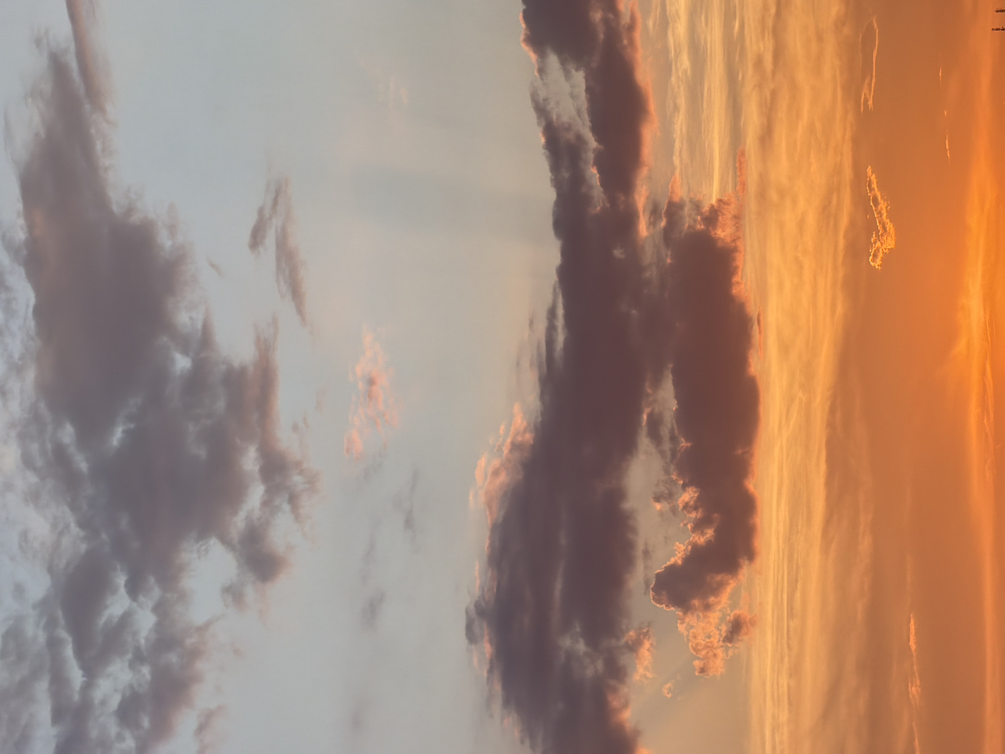 This is a vertical, wide-angle photograph of a sunset sky over Petrovac centar, Montenegro. The sky is filled with dramatic clouds, painted in hues of orange, pink, and purple.
The clouds are dense and textured, with some appearing dark and heavy while others are illuminated by the setting sun, creating a striking contrast. Rays of light are visible, suggesting the sun is low on the horizon. The overall atmosphere is serene and awe-inspiring, conveying a sense of natural beauty.
The time of day is clearly sunset, indicated by the warm, golden light and the long shadows (though no distinct shadows are visible due to the cloud cover). There are no people or man-made objects clearly visible in the frame, focusing entirely on the celestial display. The location cues are limited to the information provided in the prompt.
There is no visible text in the image.