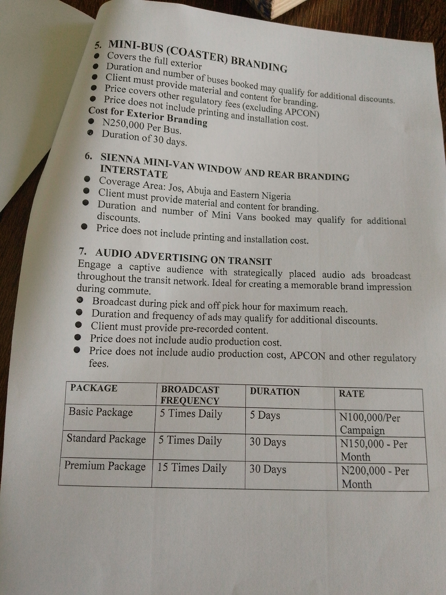 The image shows a document with text and a table. The text details advertising services, including "MINI-BUS (COASTER) BRANDING" and "SIENNA MINI-VAN WINDOW AND REAR BRANDING." It also outlines "AUDIO ADVERTISING ON TRANSIT." A table at the bottom lists packages for audio advertising, including "Basic Package," "Standard Package," and "Premium Package," with their broadcast frequency, duration, and rates. The document appears to be a service or pricing guide for advertising. There is no information within the image that mentions or suggests the location in the city of Barikin Jirga Summa, Nigeria. The image is a close-up of a printed document, likely a brochure or a page from a book.