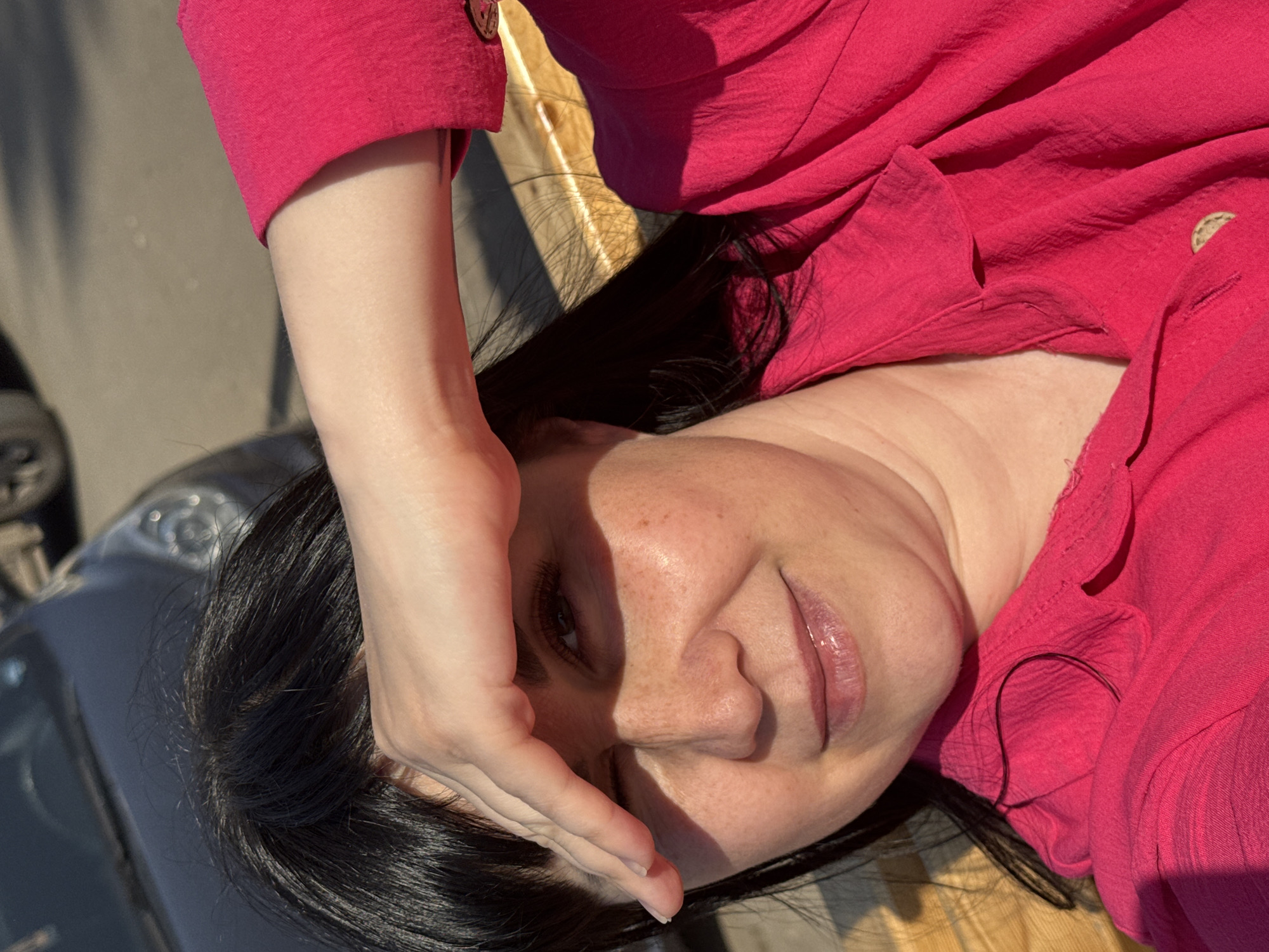 A woman lies on her back, shielding her eyes from the sun with her hand. She is wearing a pink blouse and has black hair. The background appears to be an outdoor setting, potentially a vehicle or street. No specific details indicate Zav'yalovo, Russia.