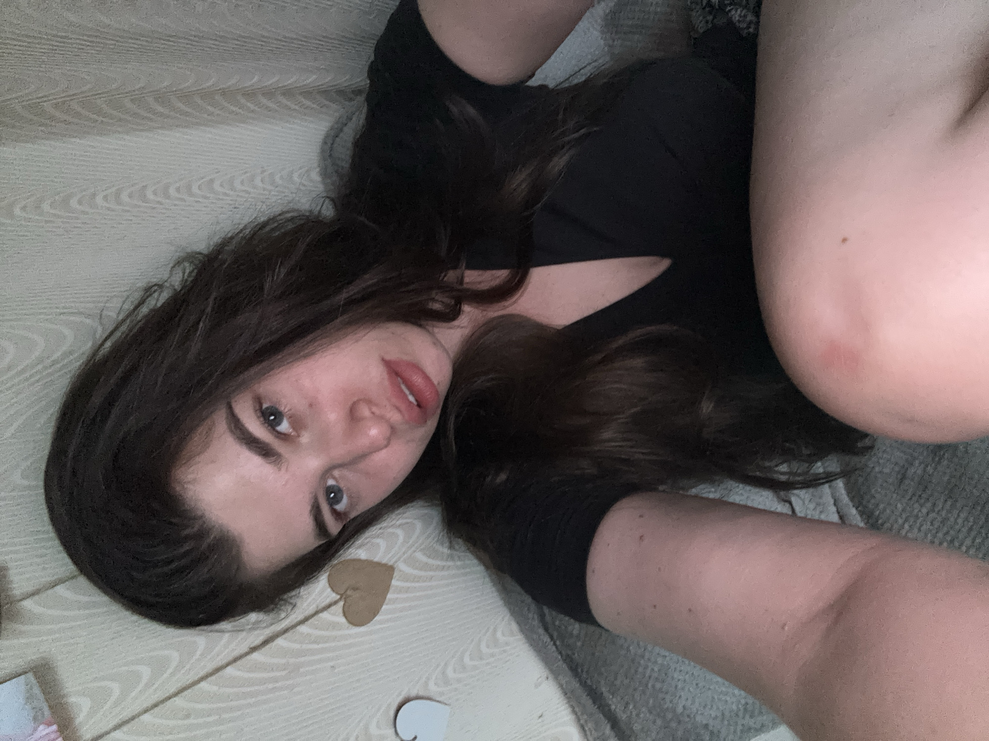 A woman with dark hair is lying on a light-colored, patterned floor. She is wearing a black top. Part of her body is resting on a gray surface. On the floor are small, cut-out heart shapes. There is no indication of the city of Мещёры, Russia.
