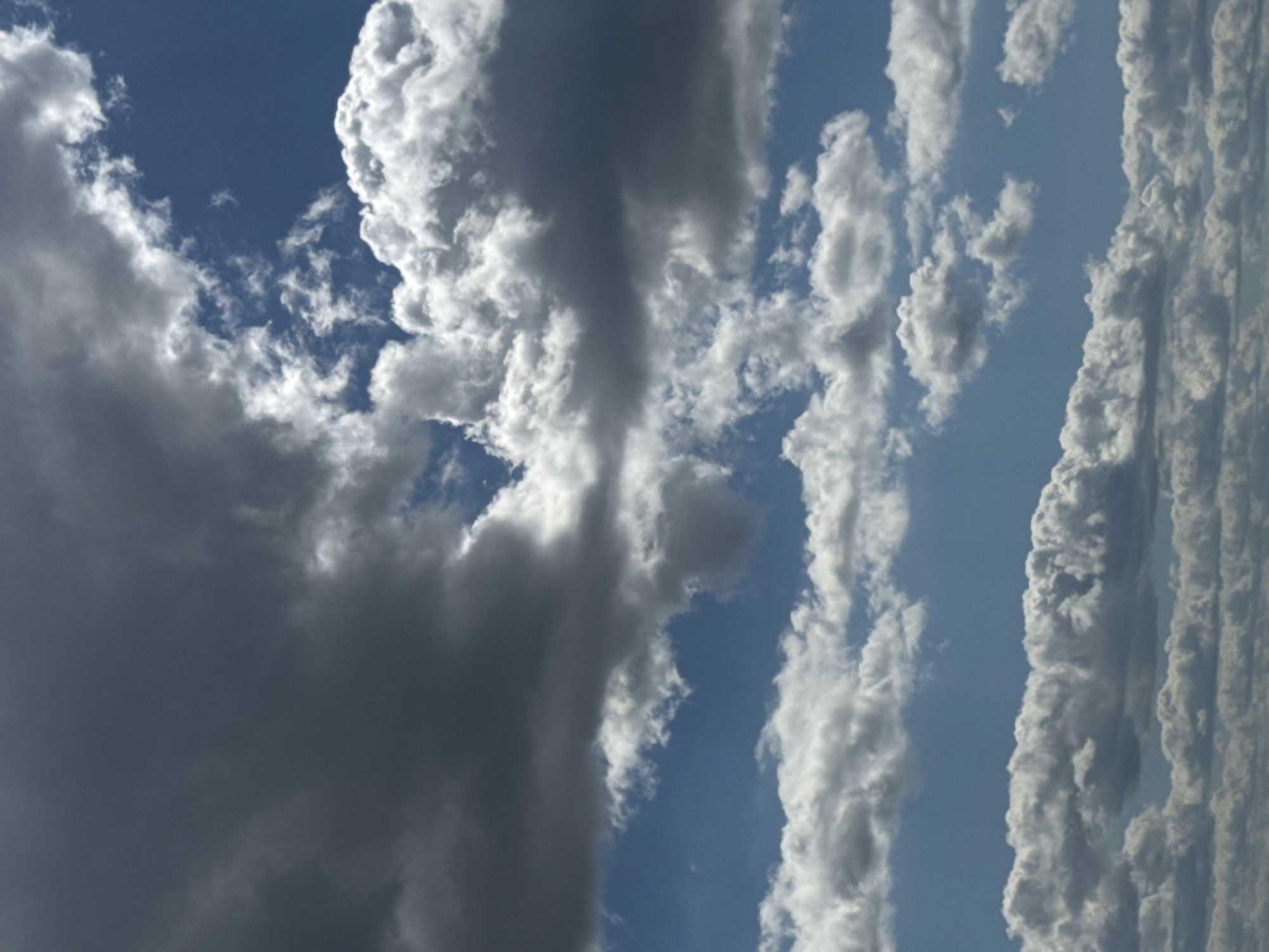This media file shows a dramatic skyscape with a variety of clouds. The dominant subjects are formations of cumulus clouds, some dark and heavy with what appears to be rain, and others bright white and fluffy. The clouds are arranged in distinct masses, with a large, dark cloud dominating the left side of the frame, and lighter, more textured clouds stretching vertically on the right. The background is a clear blue sky, suggesting it is daytime.
The weather appears to be dynamic and possibly unsettled, given the presence of the dark storm cloud. The light suggests it is daytime, with the sun likely high in the sky, illuminating the edges of the white clouds. There are no specific location cues in the image itself, but the provided location context is Акцябрскі сельскі Савет, Belarus. No people or man-made objects are visible, and there is no visible text. The scene evokes a sense of the power and beauty of nature, with the contrasting cloud formations creating a visually striking image.