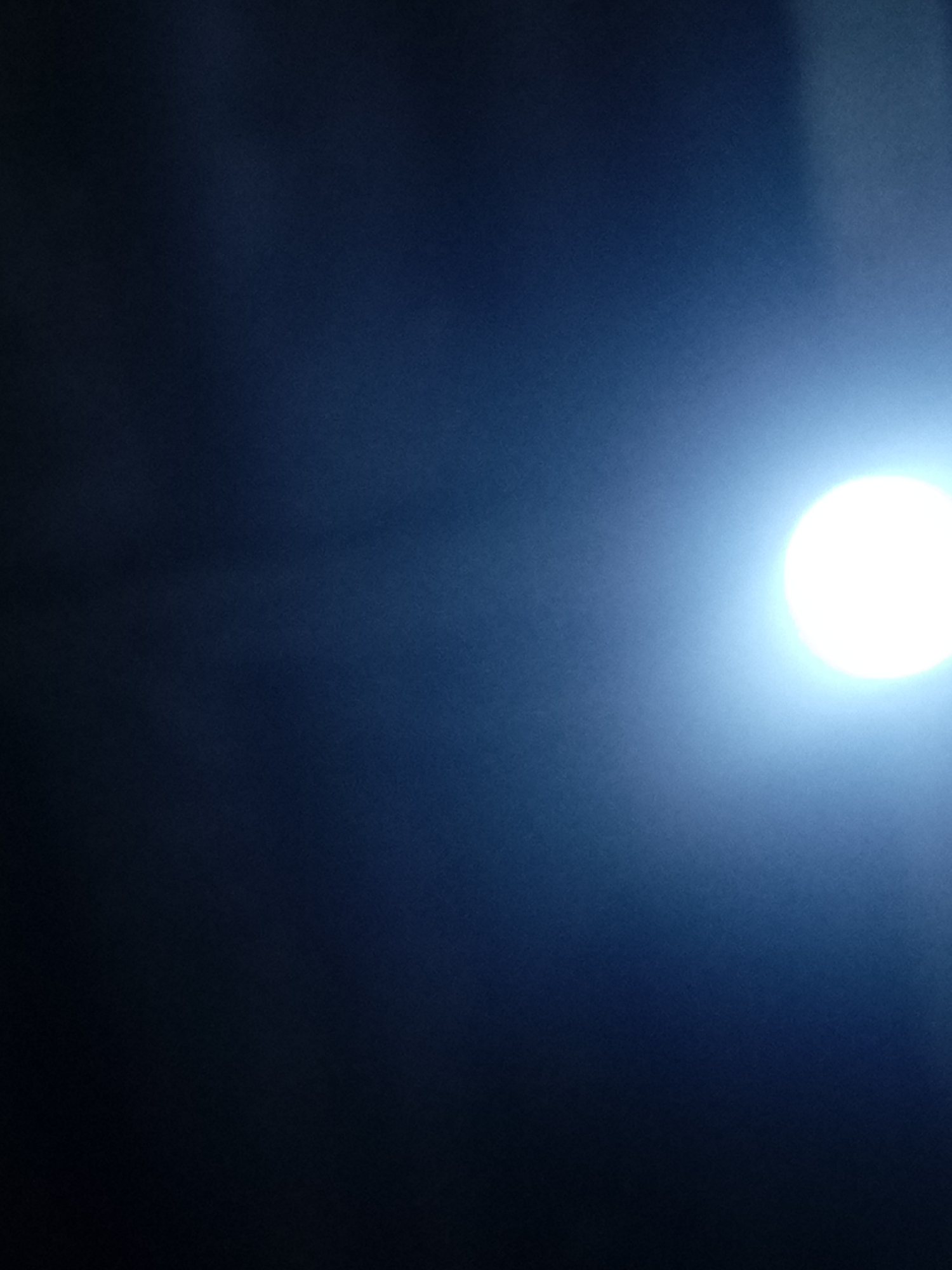 The image shows a bright, circular light source, likely the moon, positioned on the right side of the frame. The background transitions from dark on the left to a gradually lighter blue towards the right. The location of Juan Griego, Venezuela cannot be determined from the image.