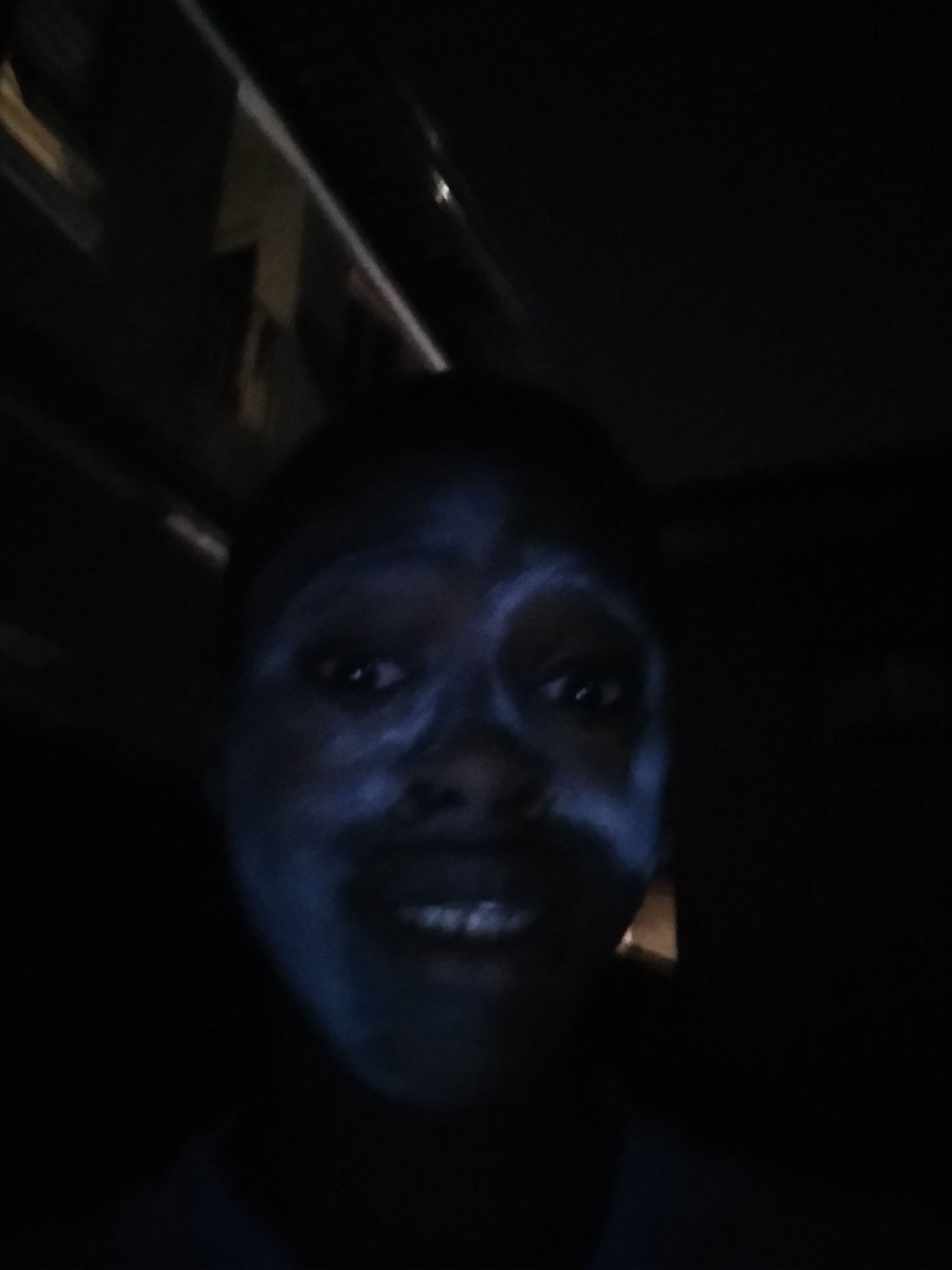 A person with a light-colored substance smeared on their face is visible in the dark. The location is the city of Shangisha, Nigeria. The environment appears to be inside a vehicle.