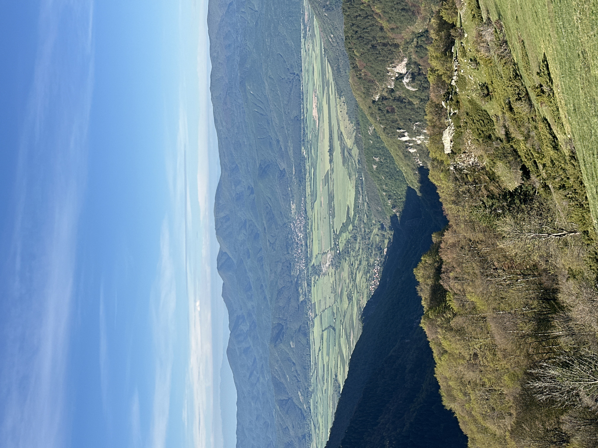 The image shows a mountain landscape near Hristo Danovo, Bulgaria. The scene features a valley with agricultural fields and a small town. Mountains rise on either side of the valley. The sky is blue with some clouds. A forested ridge is visible in the foreground.