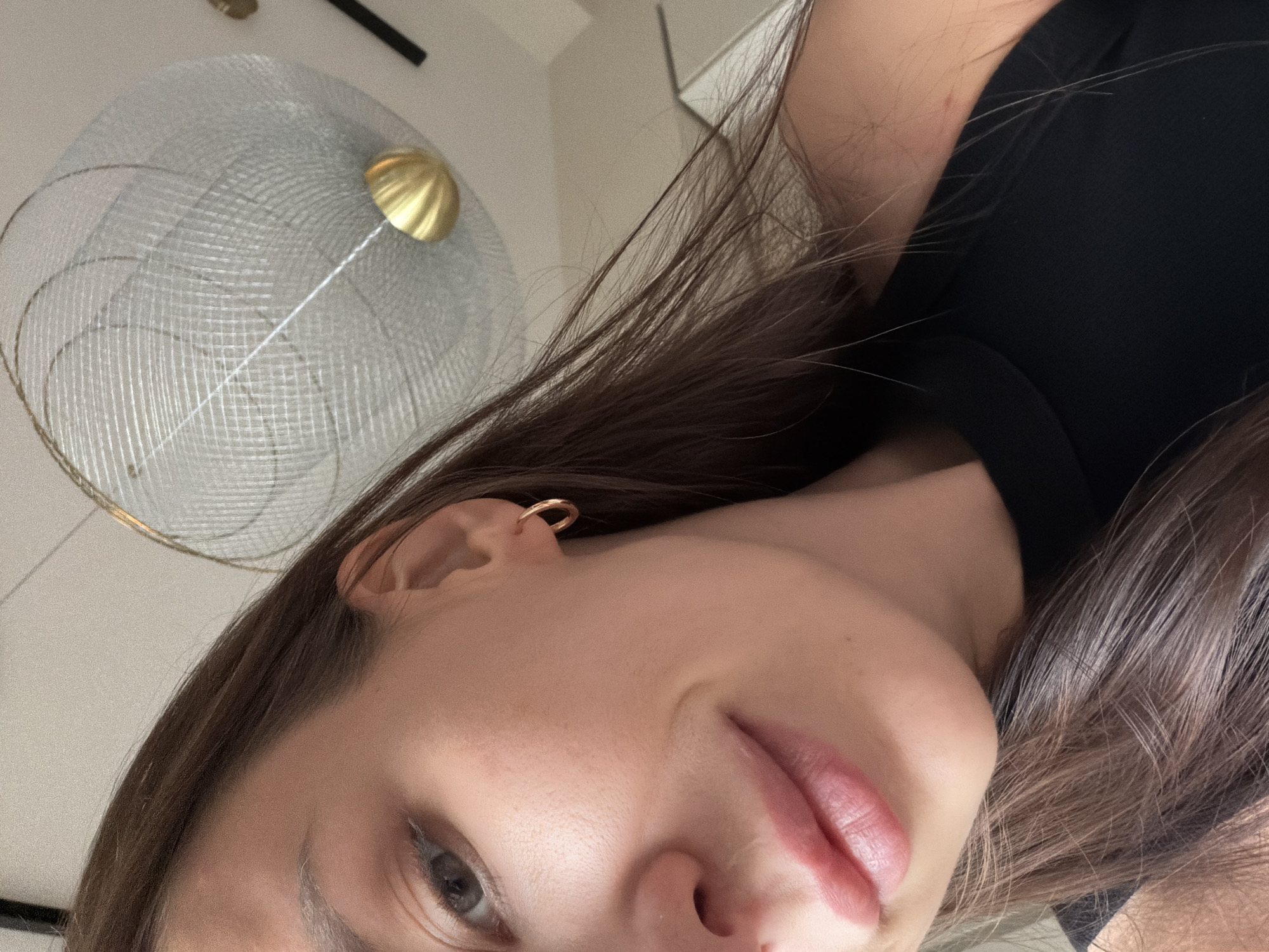 Close-up selfie of a woman with brown hair and an earring in her left ear. She is wearing a black top. In the background, out of focus, there is a decorative object resembling a wire globe with a gold colored center. The location is not identifiable as Moscow, Russia.