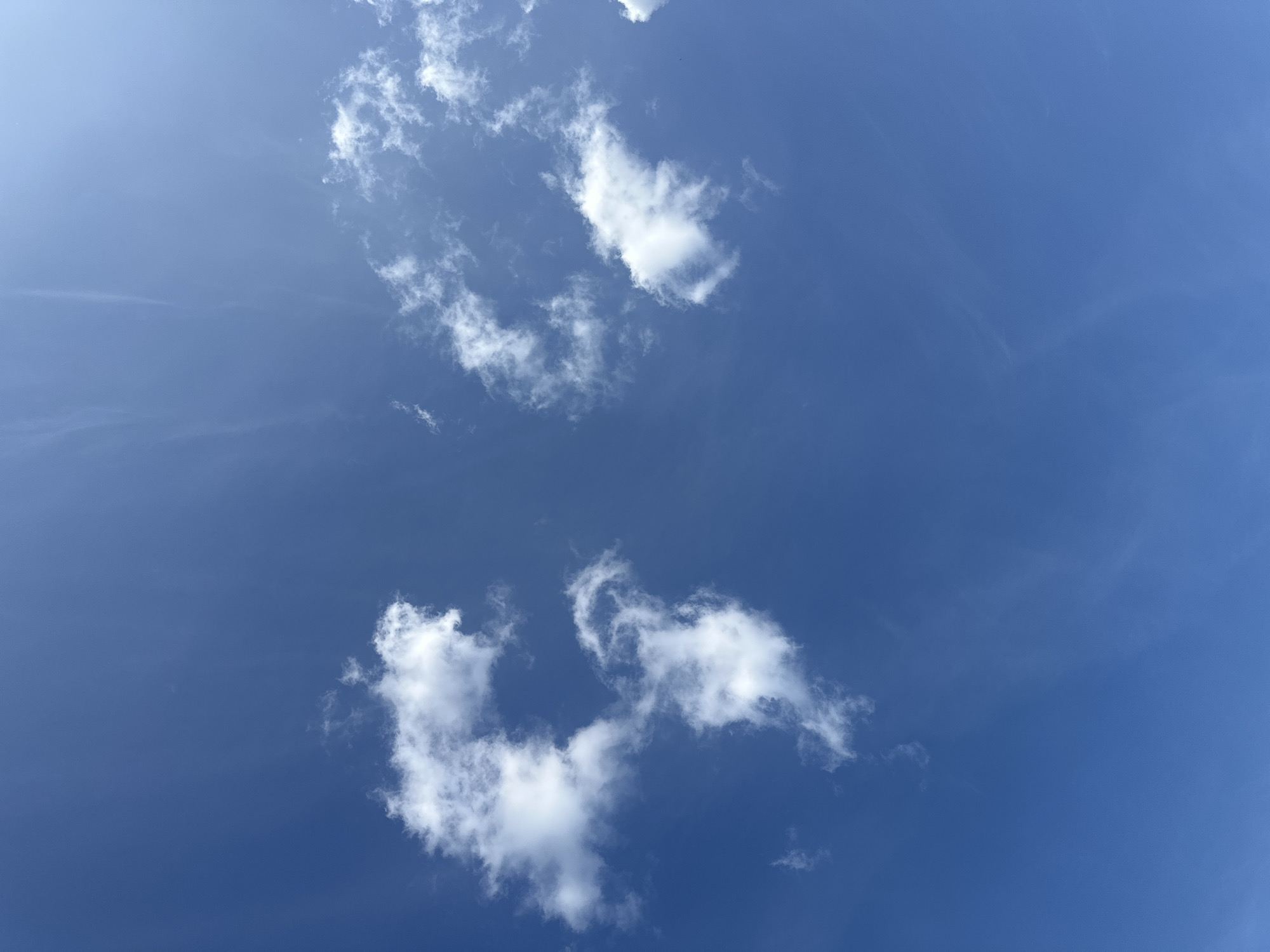 A photograph of a clear blue sky with scattered white clouds. The image captures a wide expanse of sky, with the clouds appearing as soft, fluffy formations. There is no indication of the city of Rugby, United Kingdom in this image.