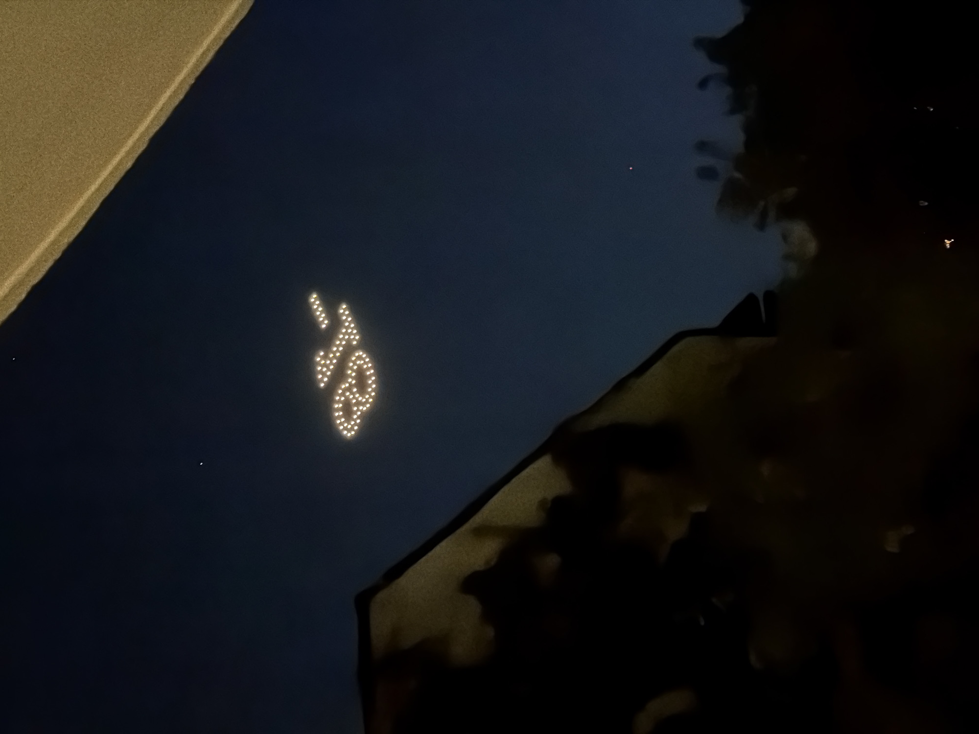At night in Sofia, Bulgaria, a drone formation in the dark sky displays the illuminated numbers "45." Part of a building is visible on the left edge, and tree branches or foliage obscure the right side.