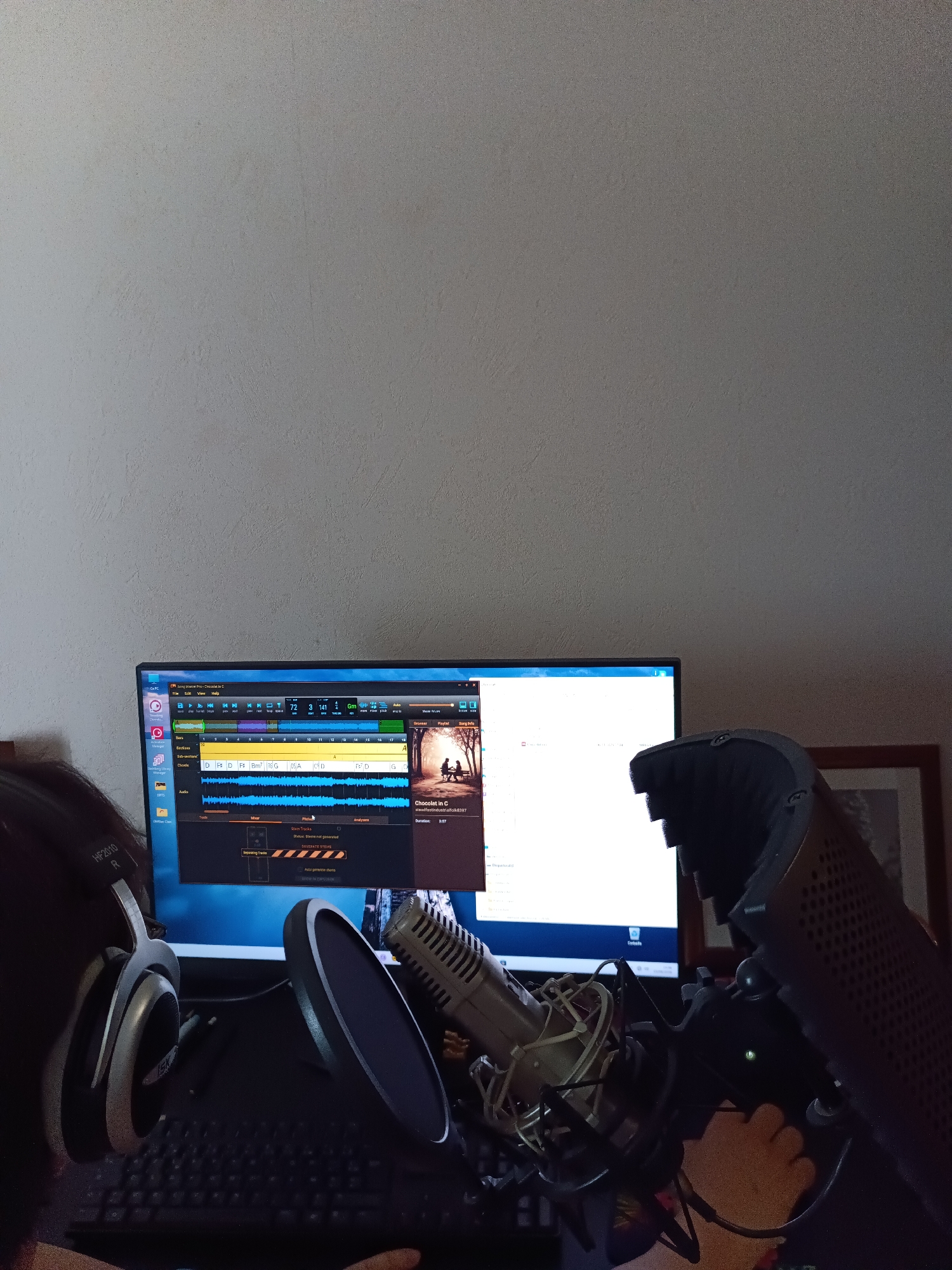 An indoor scene features a computer monitor displaying audio editing software. A microphone with a pop filter is positioned in front of the monitor, and a person wearing headphones is partially visible on the left side of the image. The monitor shows audio waveforms and track information, suggesting music production or recording activities. The background is a plain wall. The specific location within Évreux, France, cannot be determined from the image.